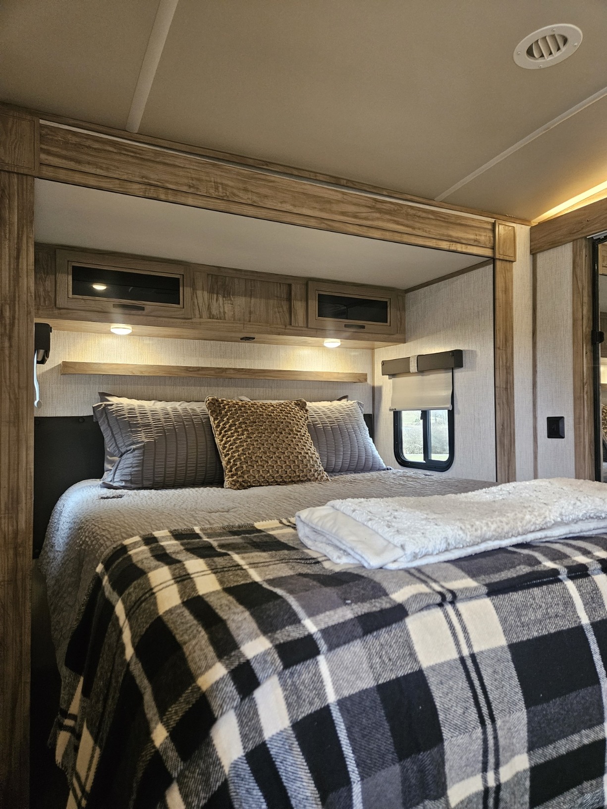 Cozy RV rental bedroom with a comfy bed, plaid blanket, and warm lighting, showcasing the comfortable sleeping area of an RV.. Forest River Palomino Solaire 2021