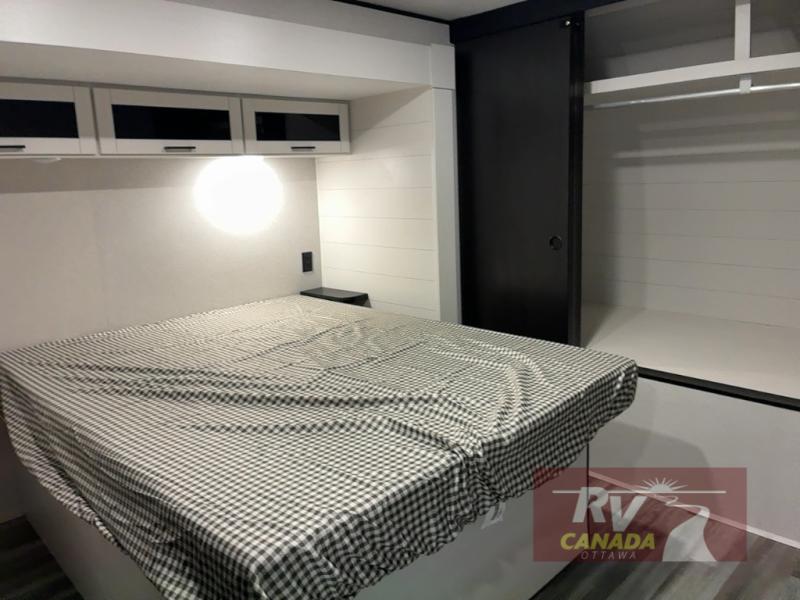Modern RV rental bedroom features a comfy bed, overhead storage, a small shelf, and a sliding closet.. Jayco Jay Flight SLX TT 2026