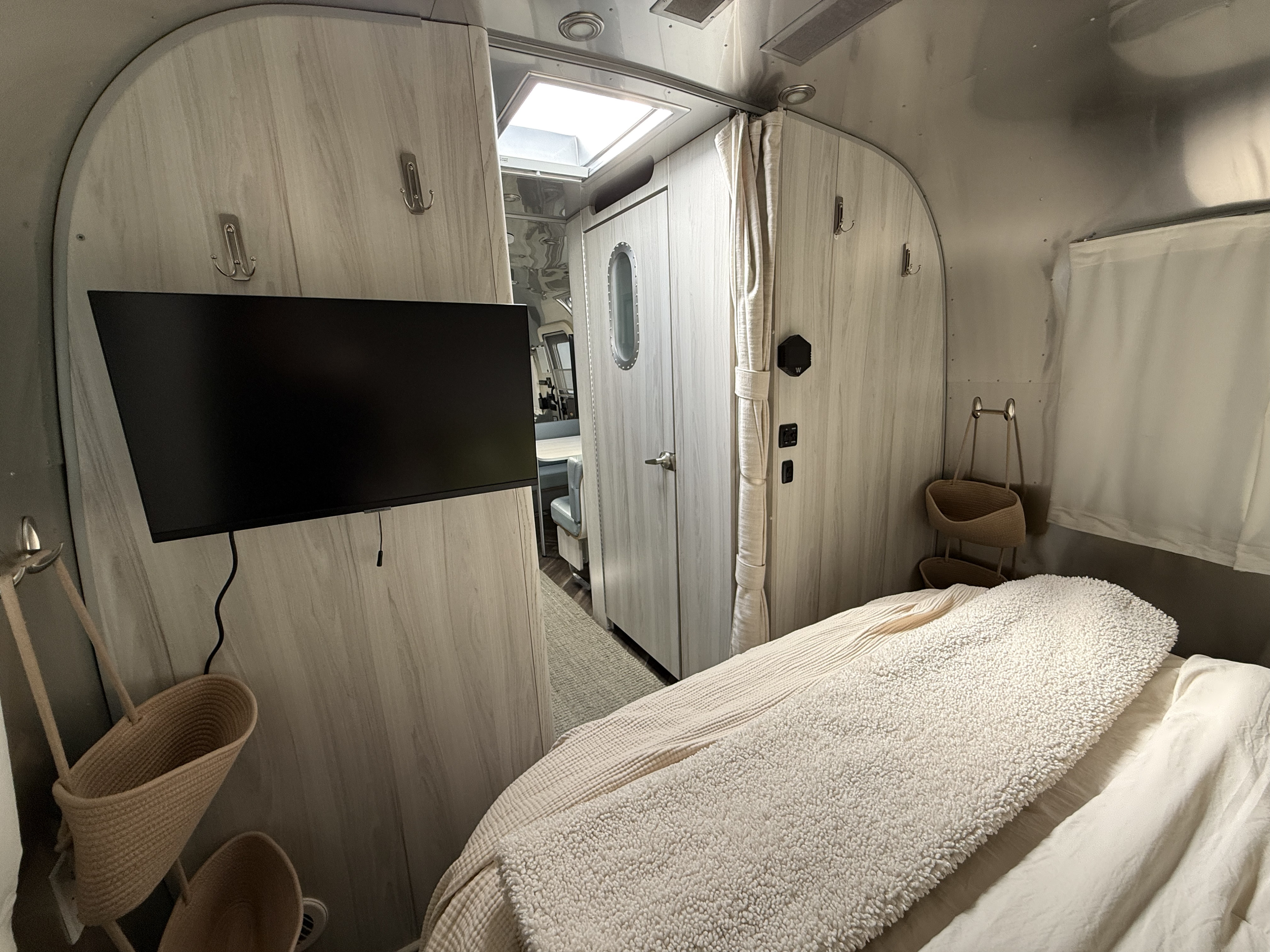 Inside a stylish RV rental, this bedroom offers a mounted TV, cozy bed with fluffy blanket, and clever storage solutions.. Airstream International 2021