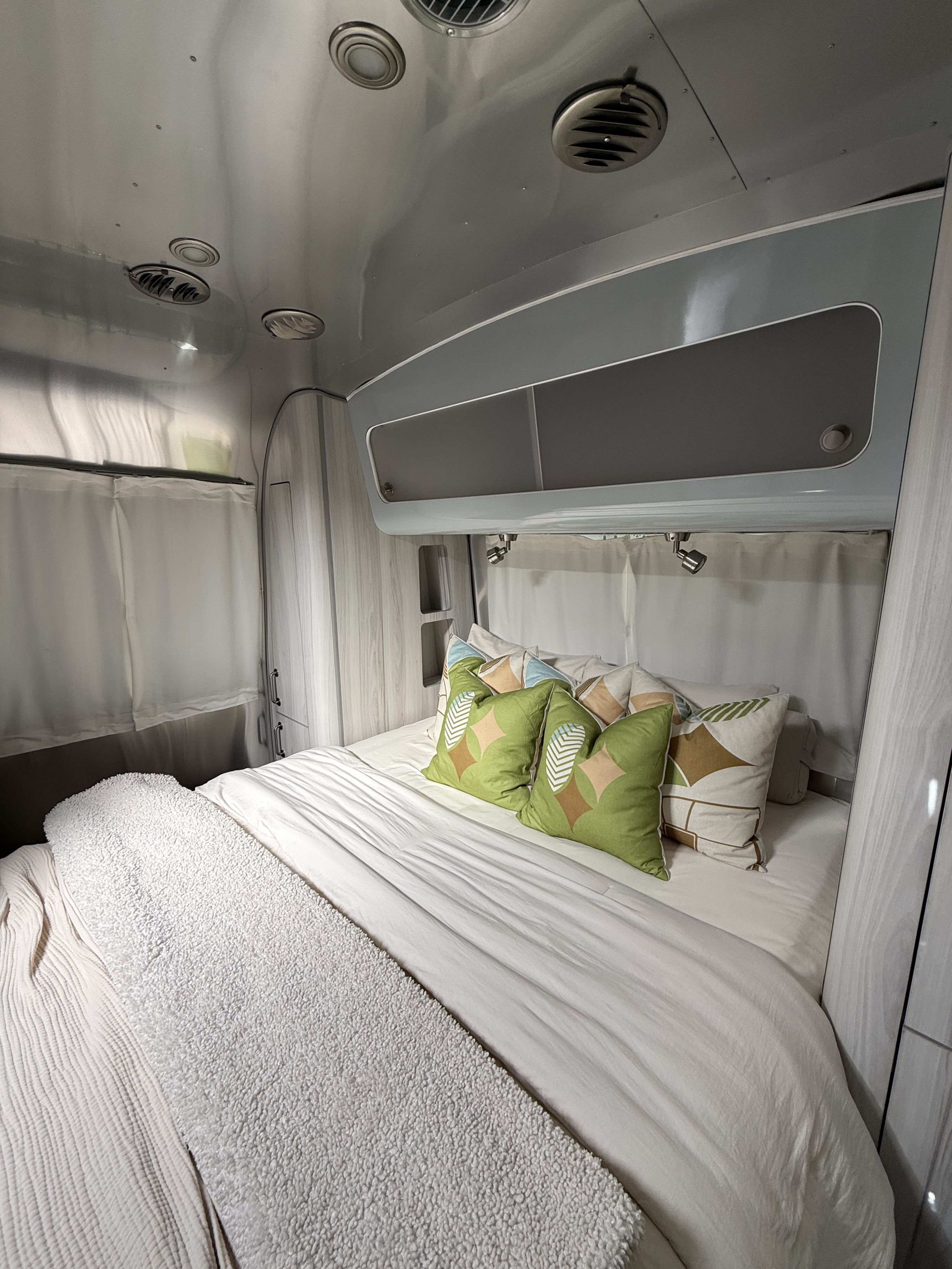 Inside an RV rental: a modern bedroom featuring a comfortable bed with colorful pillows, overhead storage, and sleek design.. Airstream International 2021