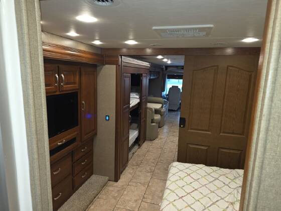 RV rental interior: A hallway leads past a TV, bunk beds, wood cabinetry, and a cozy private bedroom with a patterned quilt.. Forest River SR 340 Legacy 2018
