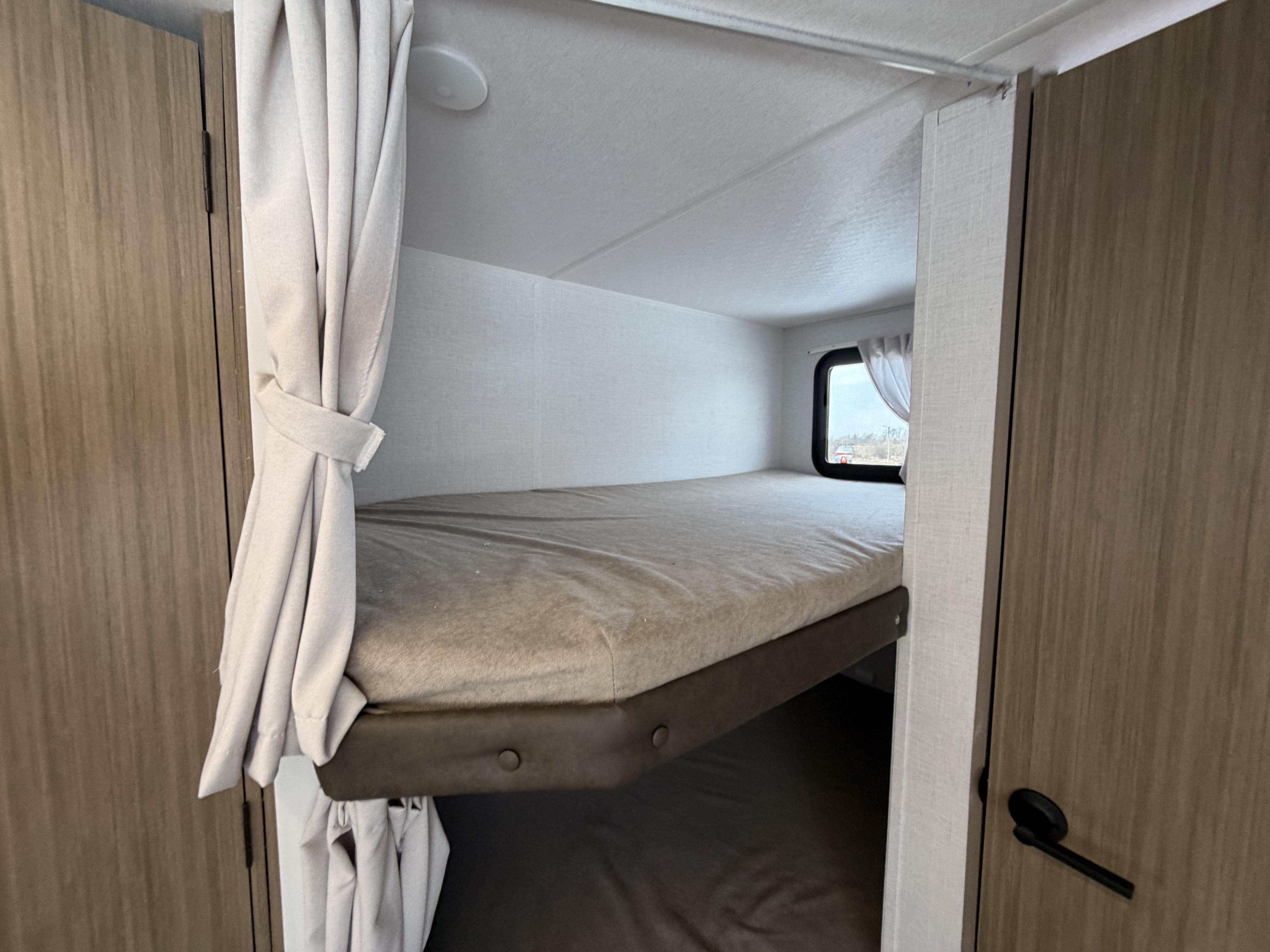 Inside an RV rental, this clean bunk bed has a light mattress, window, and privacy curtain for a comfortable stay.. Forest River Wildwood 2025