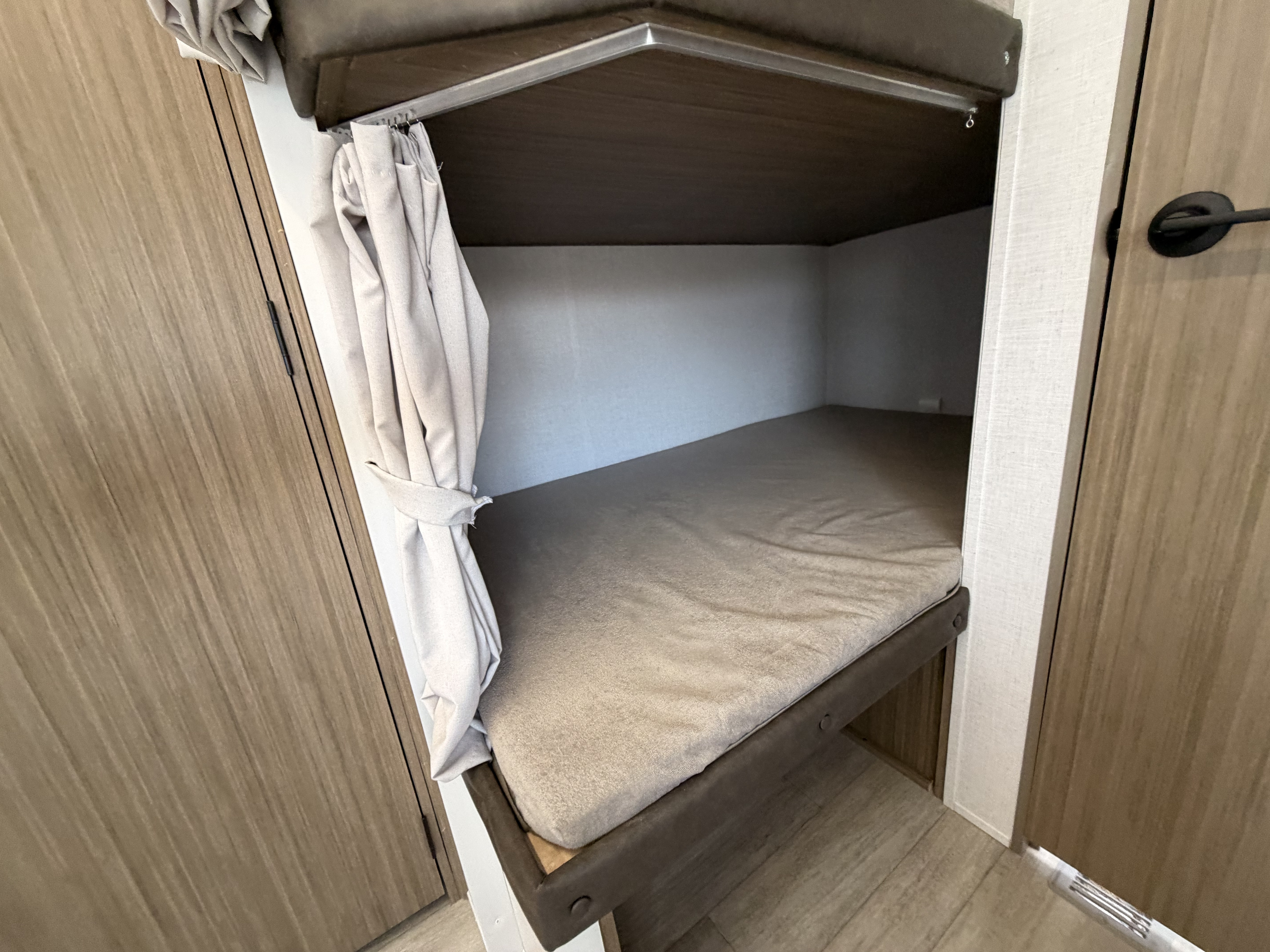 RV rental bunk bed features a cozy mattress, dark wood frame, and privacy curtain, ideal for compact sleeping areas.. Forest River Wildwood 2025