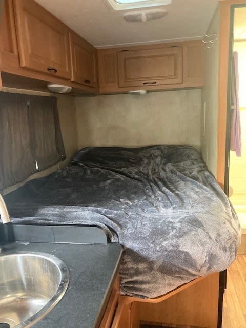 Cozy RV rental bedroom: a grey-covered bed, light wood cabinets, and a dark counter with a sink.. Thor Majestic 2012