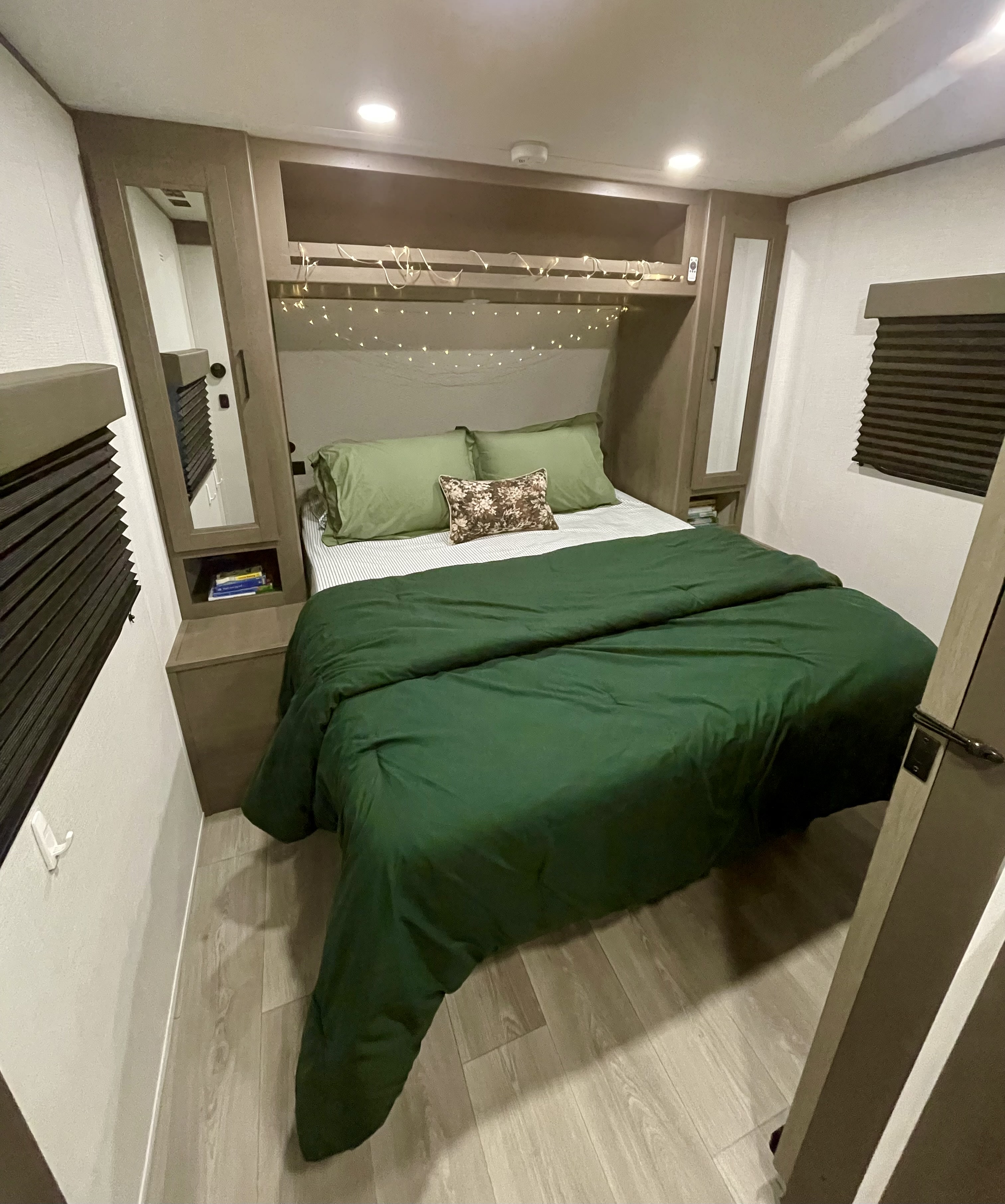 Inside an RV rental, a cozy bedroom with green bedding, fairy lights, and built-in storage, offering comfort for travelers.. Grand Design Transcend Xplor 2026