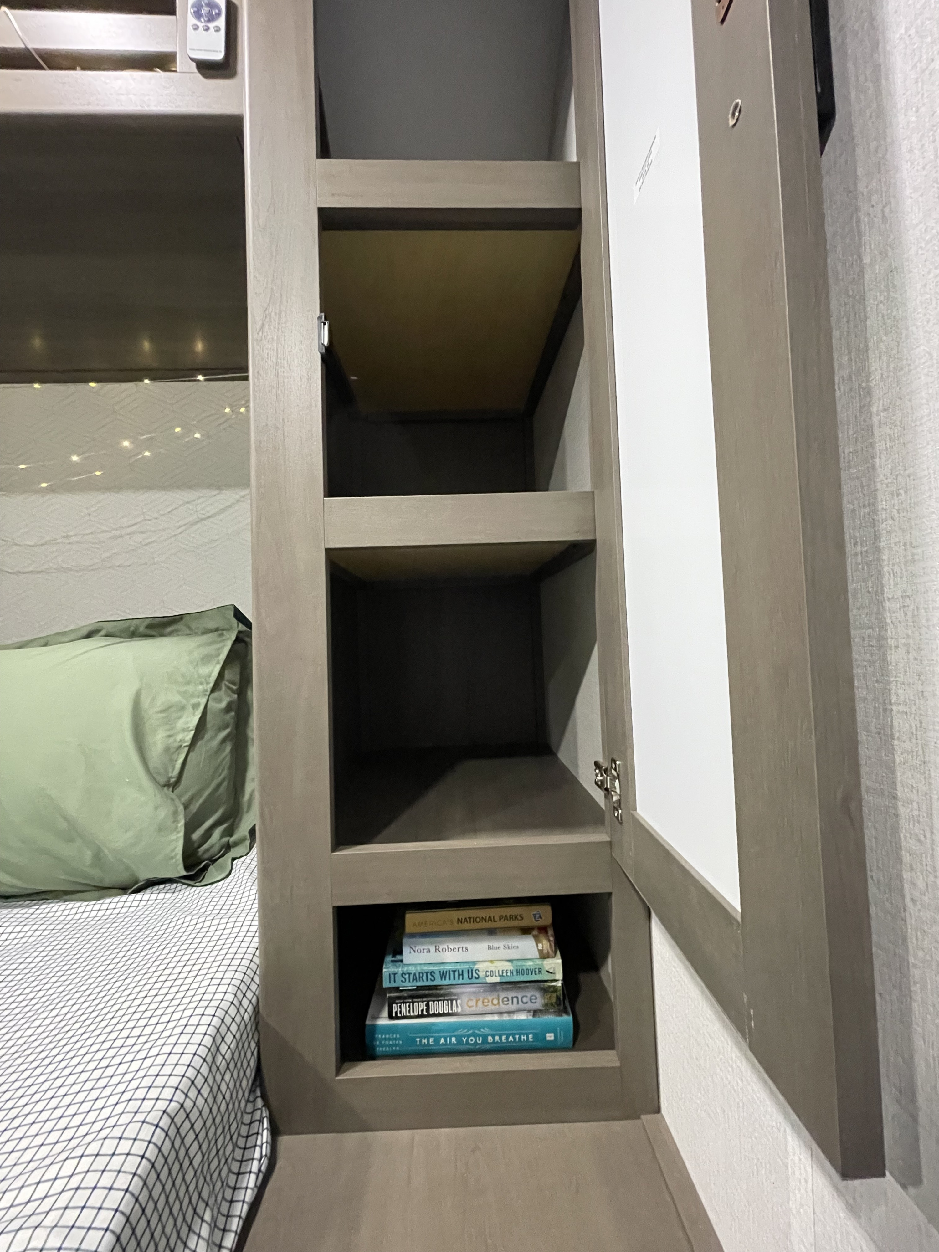 Cozy RV rental interior: A bed with string lights and built-in shelving. The bottom shelf holds books, while other shelves provide storage.. Grand Design Transcend Xplor 2026