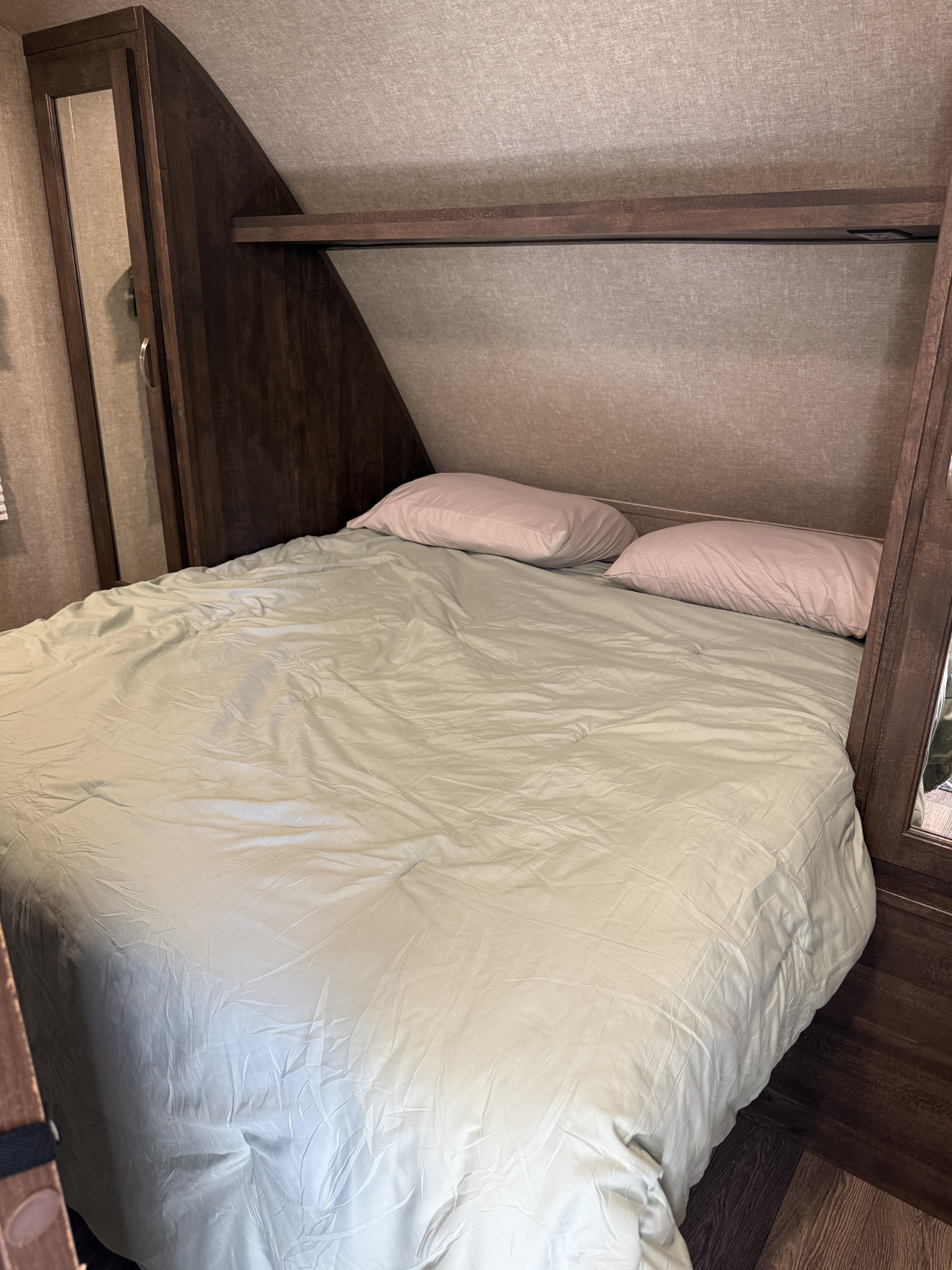 Compact RV rental bedroom featuring a bed with soft pillows, light green bedding, and built-in wooden storage.. Forest River Vibe Extreme Lite 2019