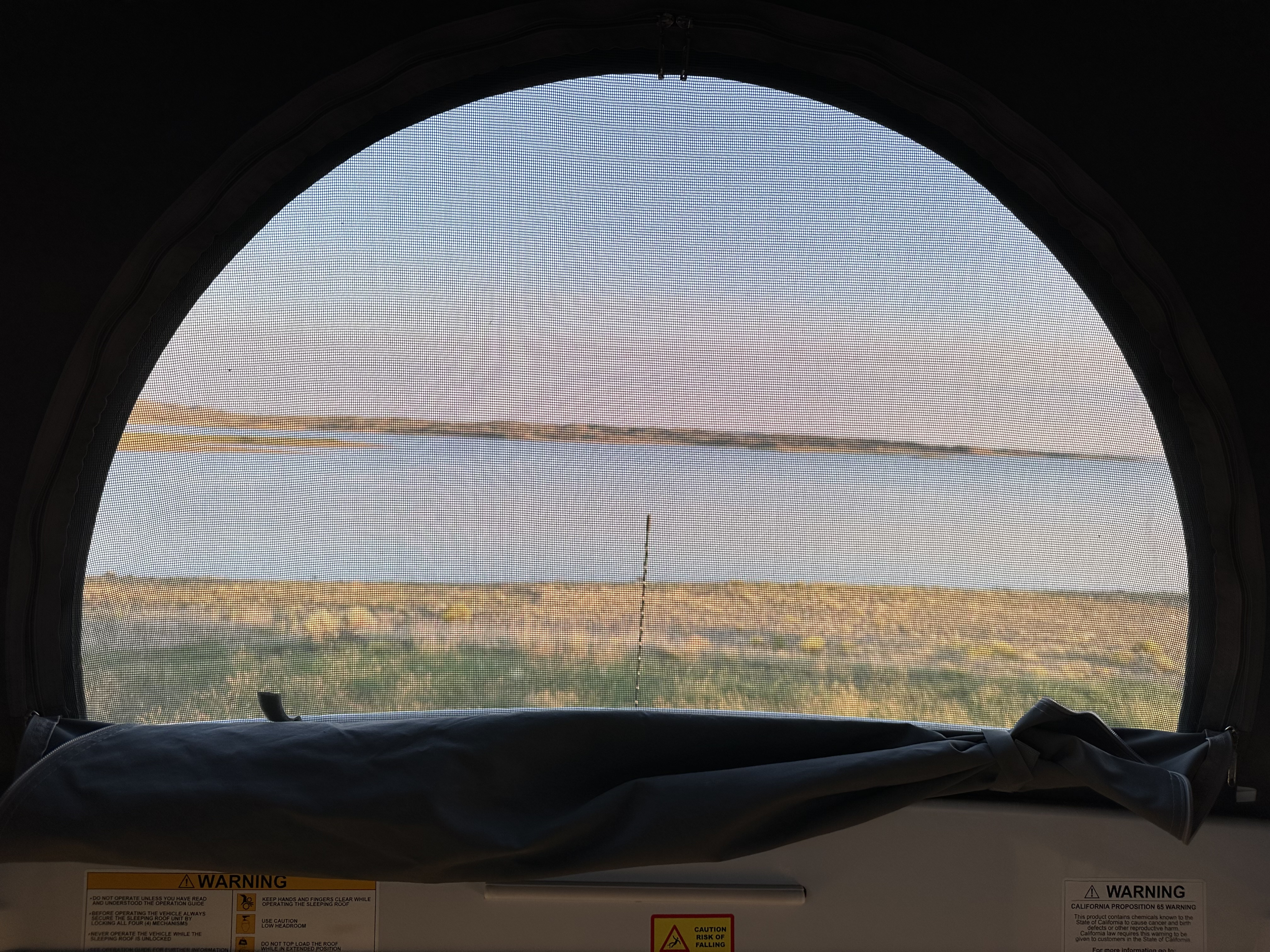 Inside an RV rental: Screened window frames a scenic lake and grassy landscape. Warning labels visible below.. Winnebago Winnebago 2022