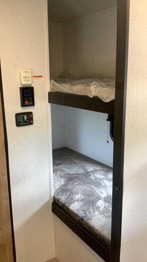 RV rental interior featuring stacked bunk beds; the top bunk mattress is still plastic-wrapped. Control panels are on the wall.. Keystone RV Springdale 2023