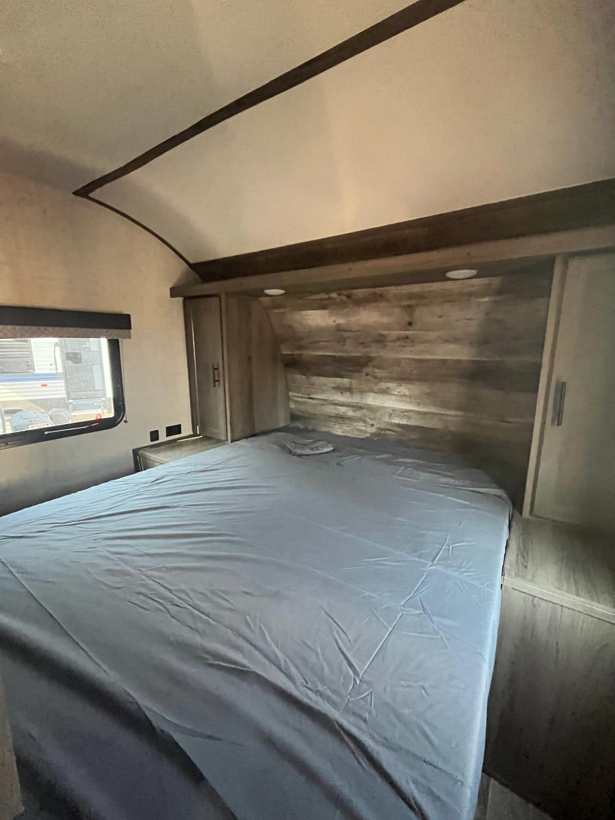 Cozy RV rental bedroom features a bed with blue sheets, wooden headboard with lights, and built-in side cabinets.. Gulf Stream Kingsport 2023