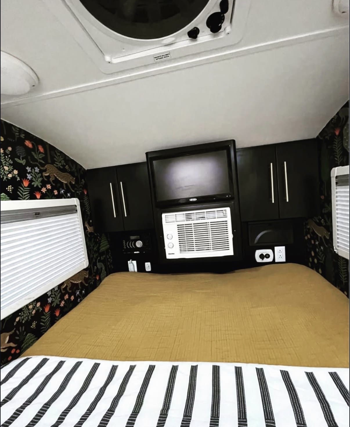 Cozy RV rental bedroom with dark jungle wallpaper, TV, AC, and a comfy mustard bed. Perfect for travel adventures!. nuCamp T@G 2017