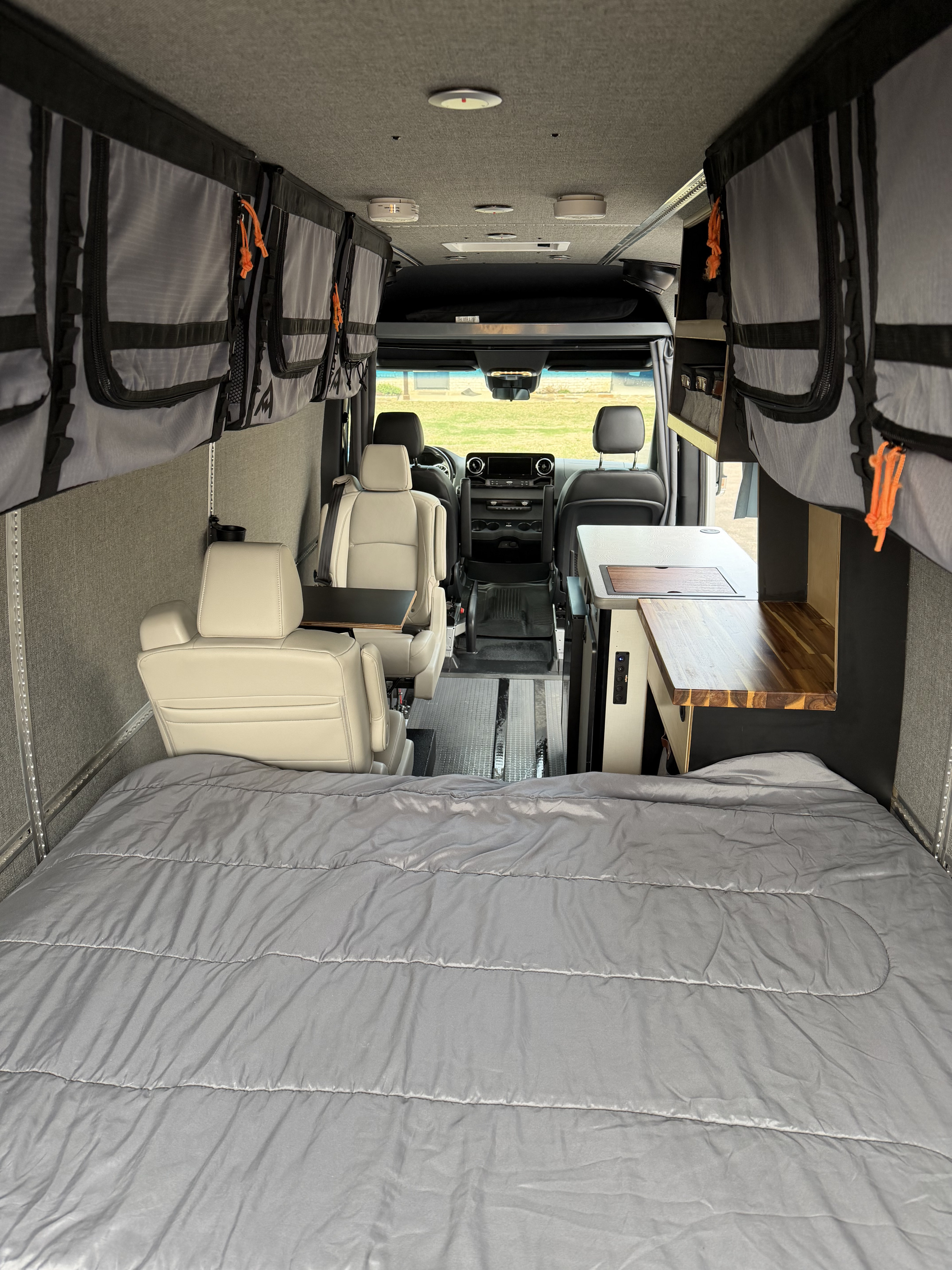 View of a well-appointed RV rental interior with a cozy bed, compact kitchen, and swiveling front seats for comfort.. Winnebago Adventure Wagon 2023
