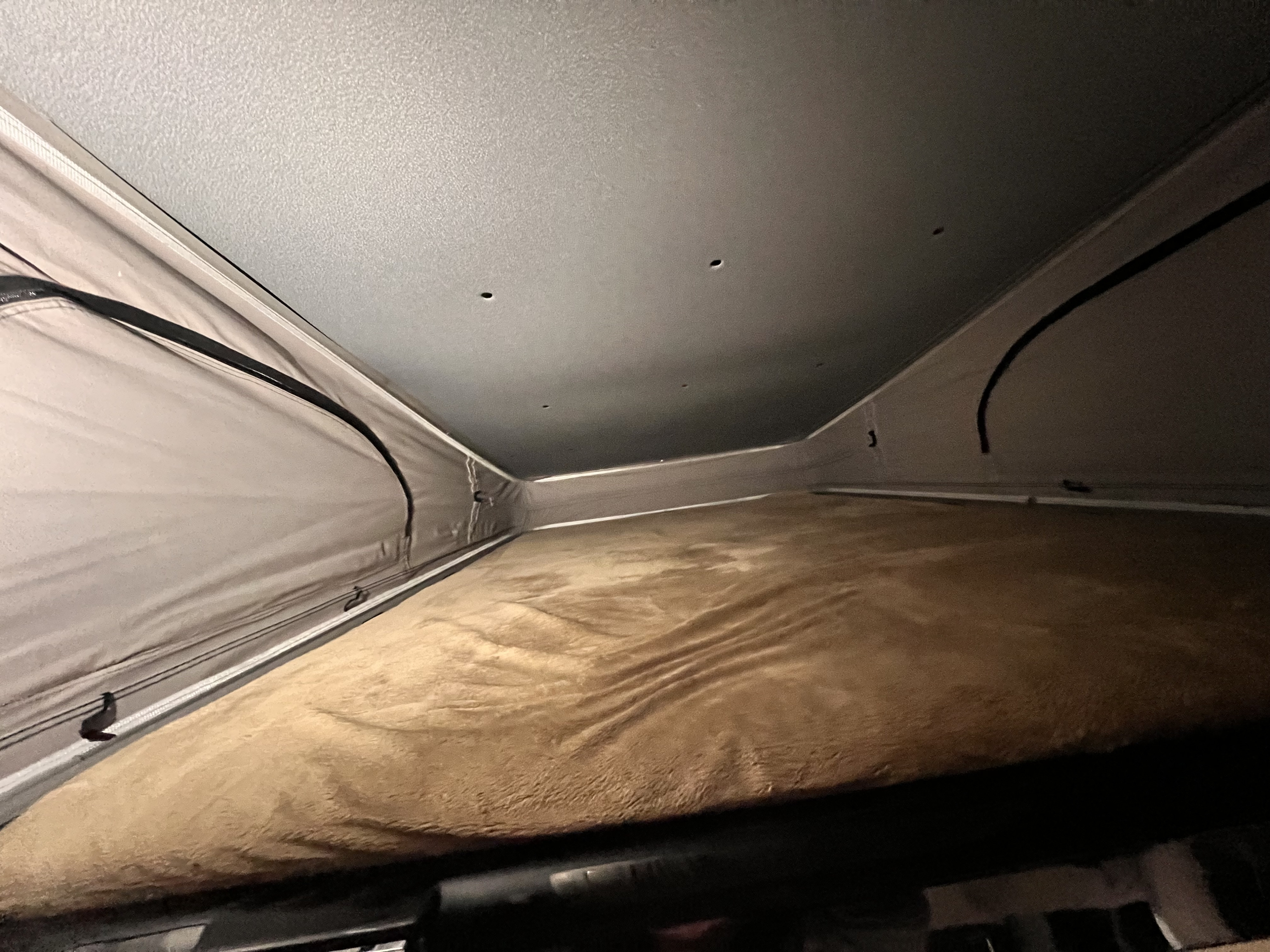 Cozy pop-top sleeping area of an RV rental with a soft brown blanket, fabric walls, and a grey ceiling, ready for rest.. Thor Rize 2022