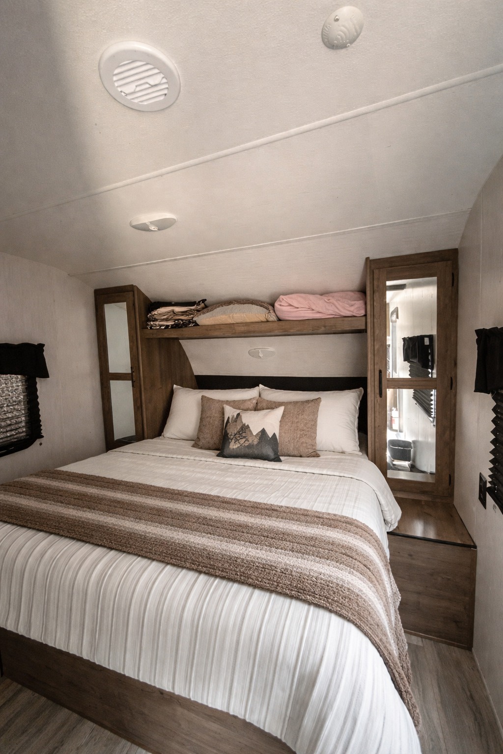 Inviting RV rental bedroom with a striped throw on a comfy bed, mountain pillow, and wood storage. Ready for your adventure.. Heartland RVs Pioneer 2023