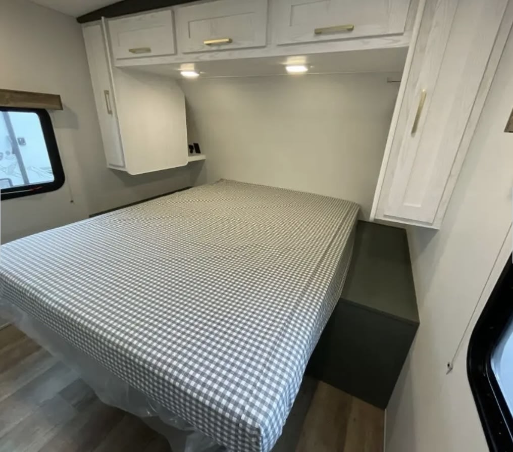 Cozy RV rental bedroom with a checkered bed, overhead cabinets, and a window. A comfortable sleeping area for your travel adventures.. Heartland RVs Eddie Bauer 2024