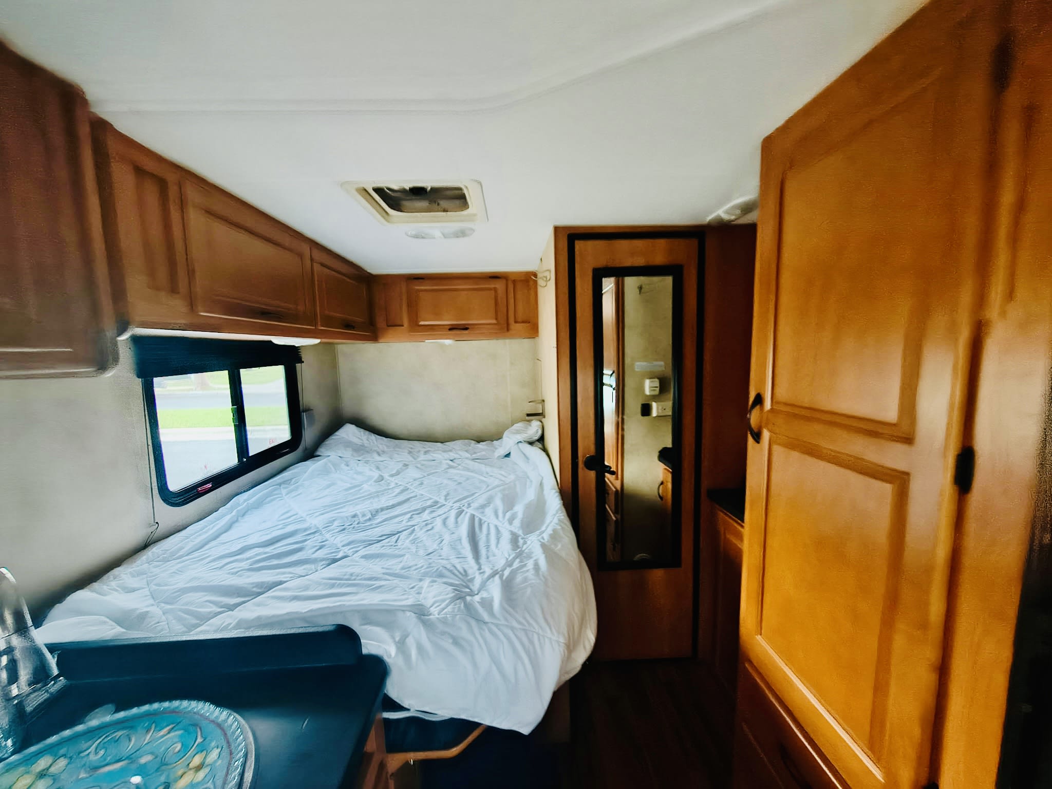 Cozy RV rental bedroom area with a neatly made bed, window, and numerous wooden storage cabinets overhead and beside.. Thor Majestic 2014