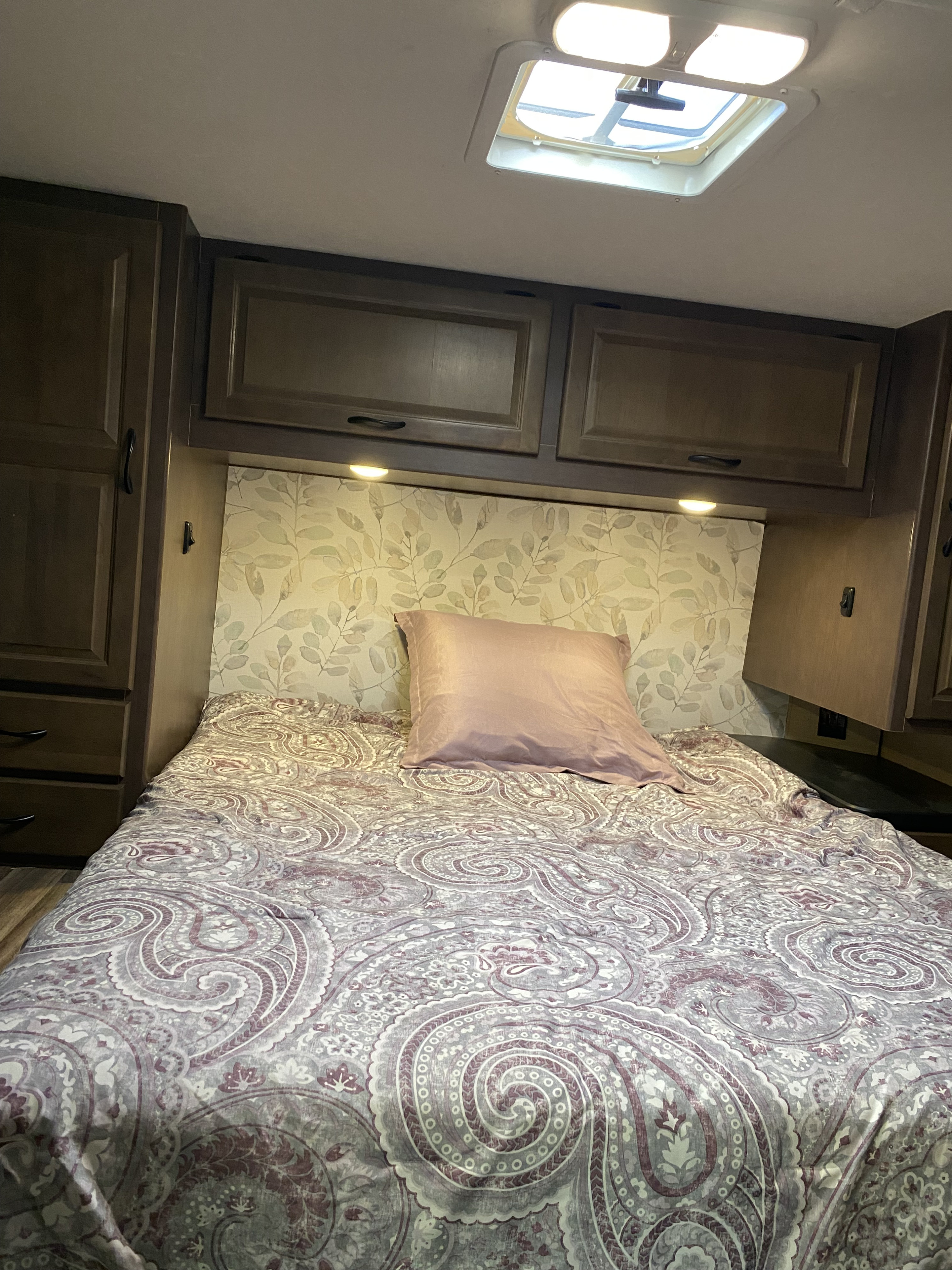 Cozy RV rental bedroom with patterned bedding, a pink pillow, dark wood cabinets, and a ceiling vent for natural light.. Thor Majestic 2018