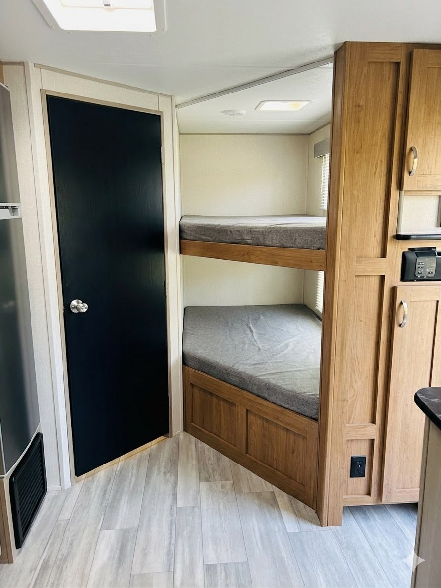 RV rental interior featuring a cozy sleeping area with bunk beds, a modern black door, and light wood cabinetry.. Forest River Tracer LE 2021
