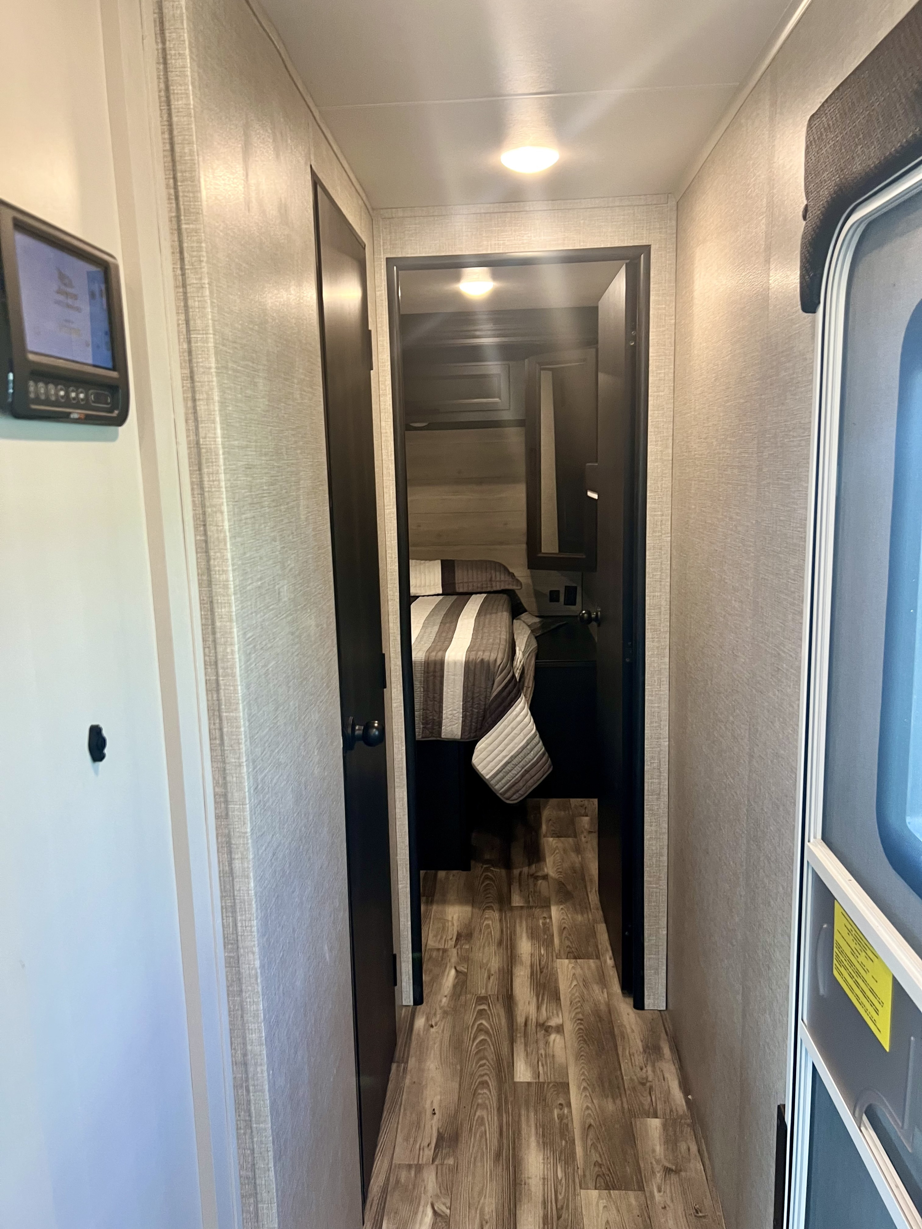 This RV rental interior shows a hallway leading to a bedroom with striped bedding. A control panel and entry door are visible.. Jayco Eagle HT 280RSOK 2023