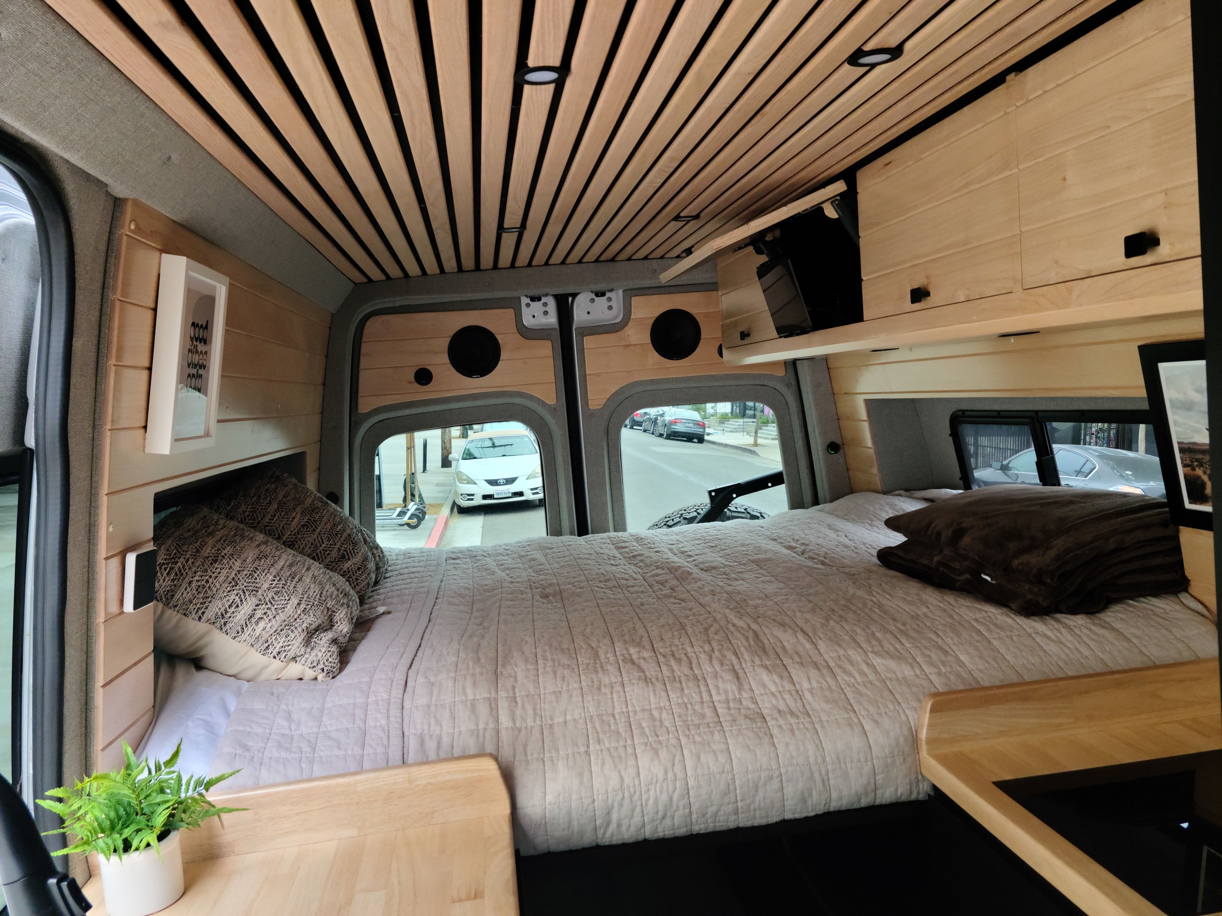 Cozy RV rental interior with a comfortable bed, wooden ceiling, and street view. Perfect for travel!. Mercedes-Benz Sprinter 2021