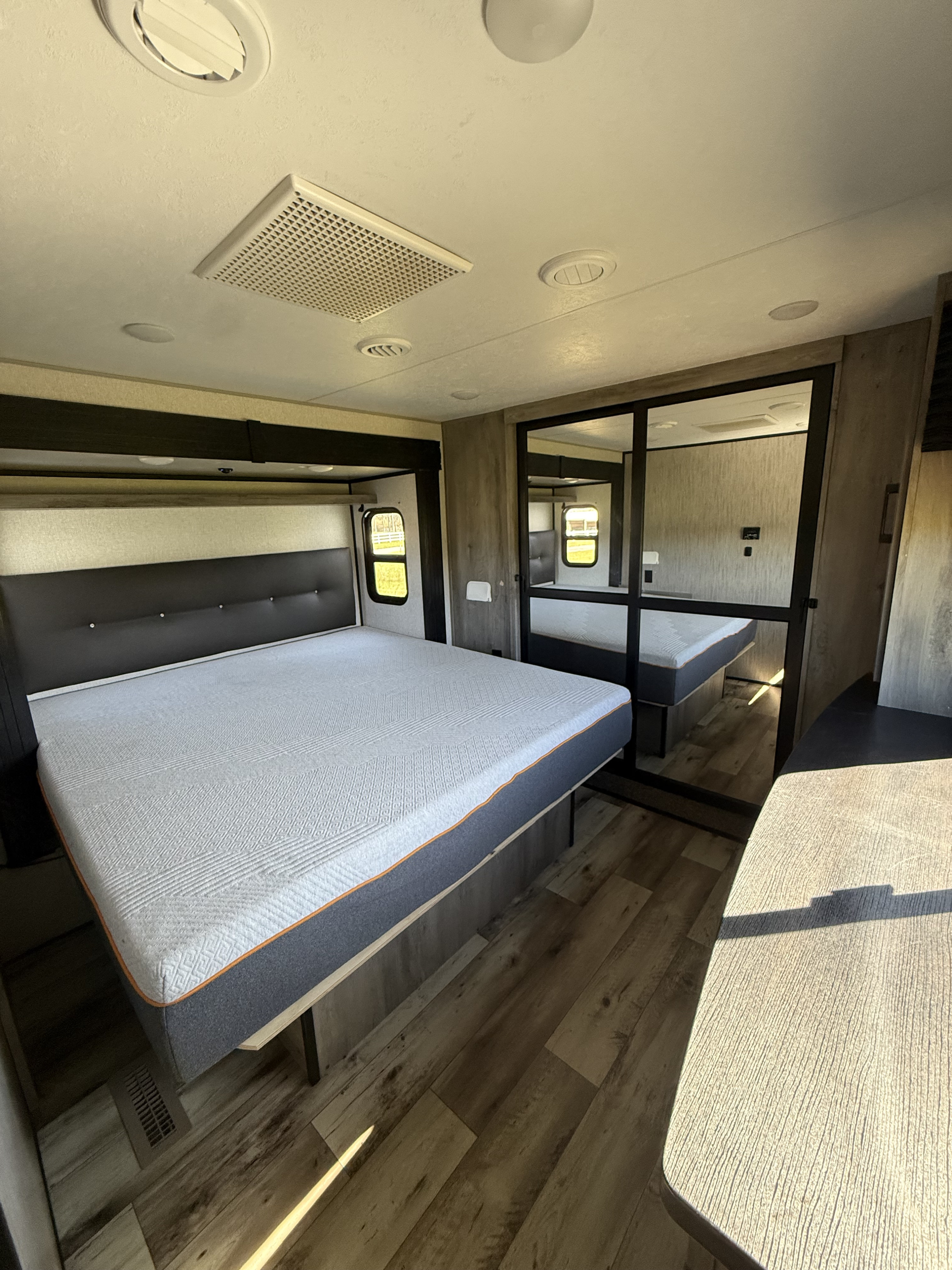 Modern RV rental bedroom featuring a large bed with a dark headboard, mirrored closet, and wood-look floor.. Durango Durango Fifth Wheel 2022