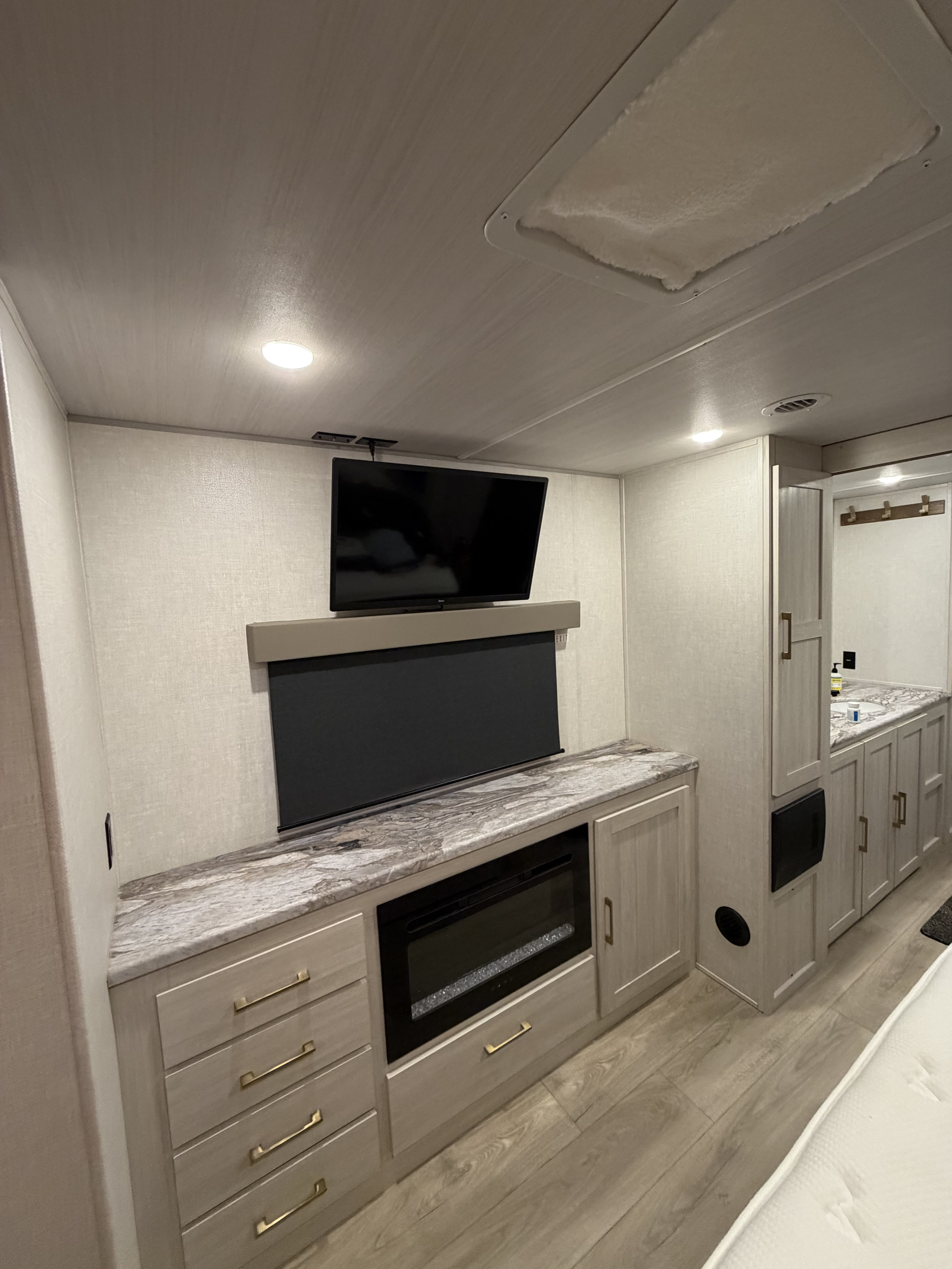 Modern rv rental interior featuring a TV, electric fireplace, built-in storage, and a partial view of a bathroom vanity.. Forest River Surveyor Land Surveyor 2024