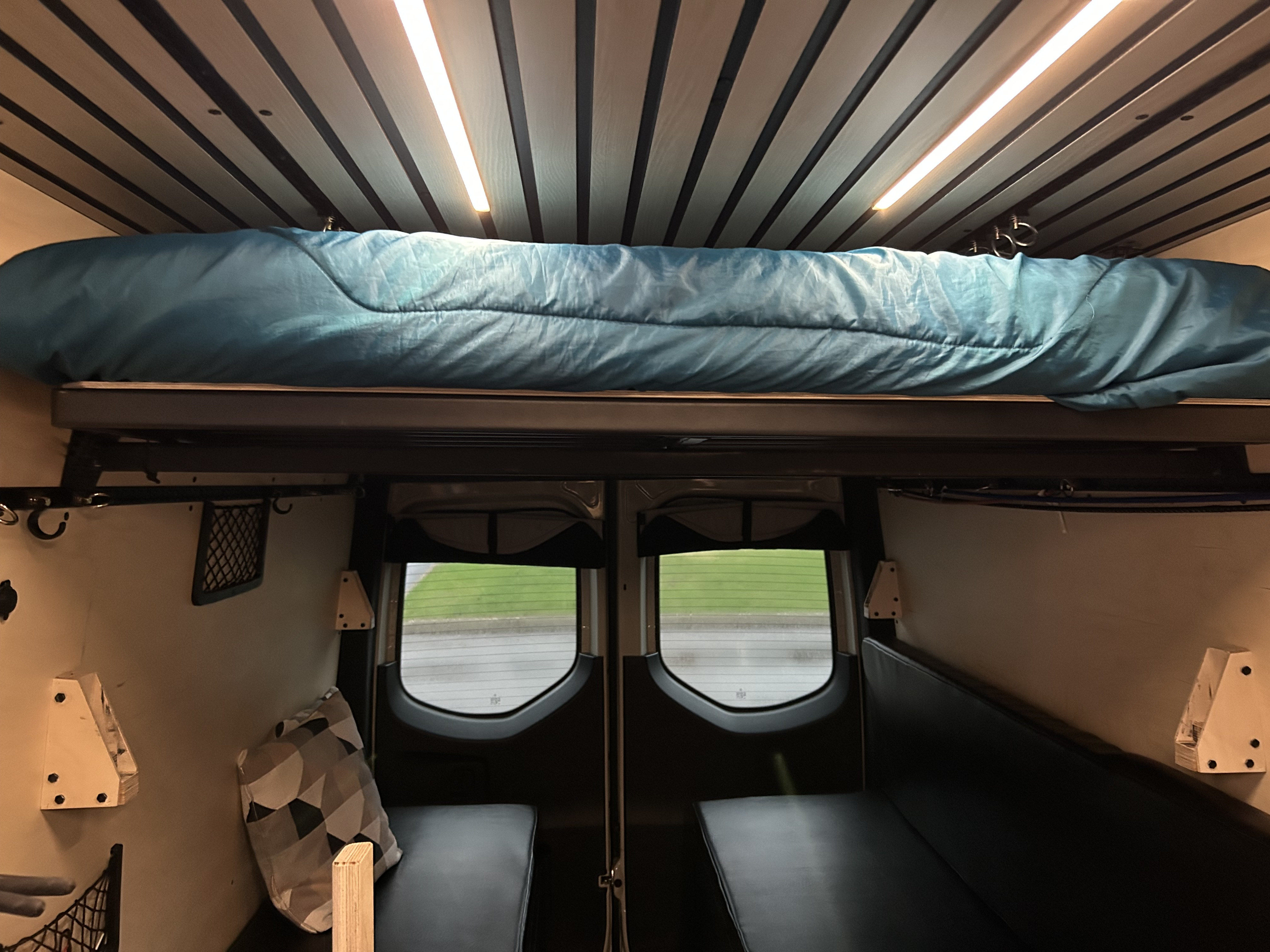 Experience comfort in this RV rental: upper bed, lower benches, rear windows, and sleek interior lighting in a campervan.. Mercedes-Benz Sprinter 2024