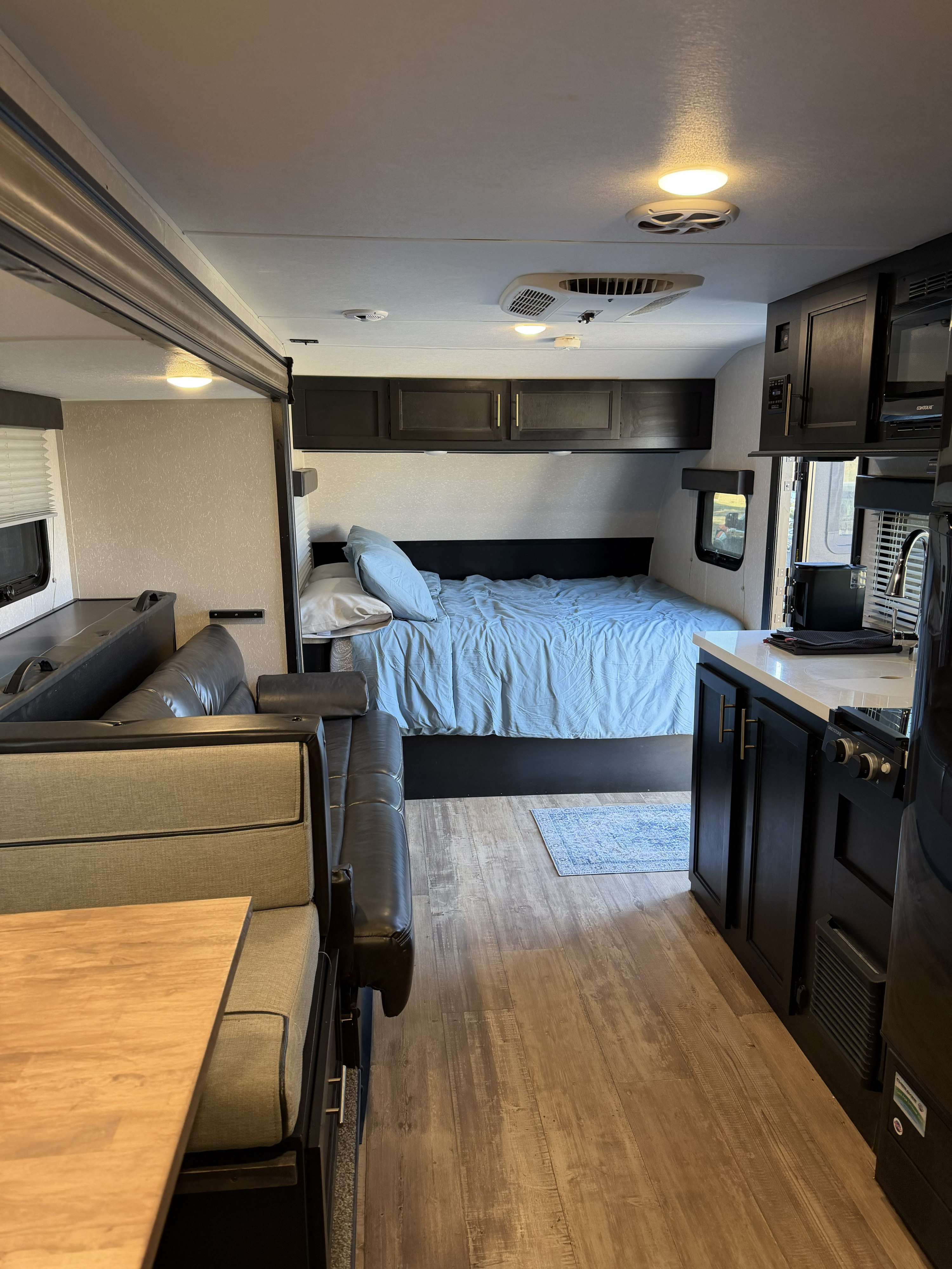 RV rental interior: A cozy bedroom with blue bedding, plus a compact kitchen and dinette area on wood-look flooring.. Forest River Cherokee Wolf Pup Black Label 2021