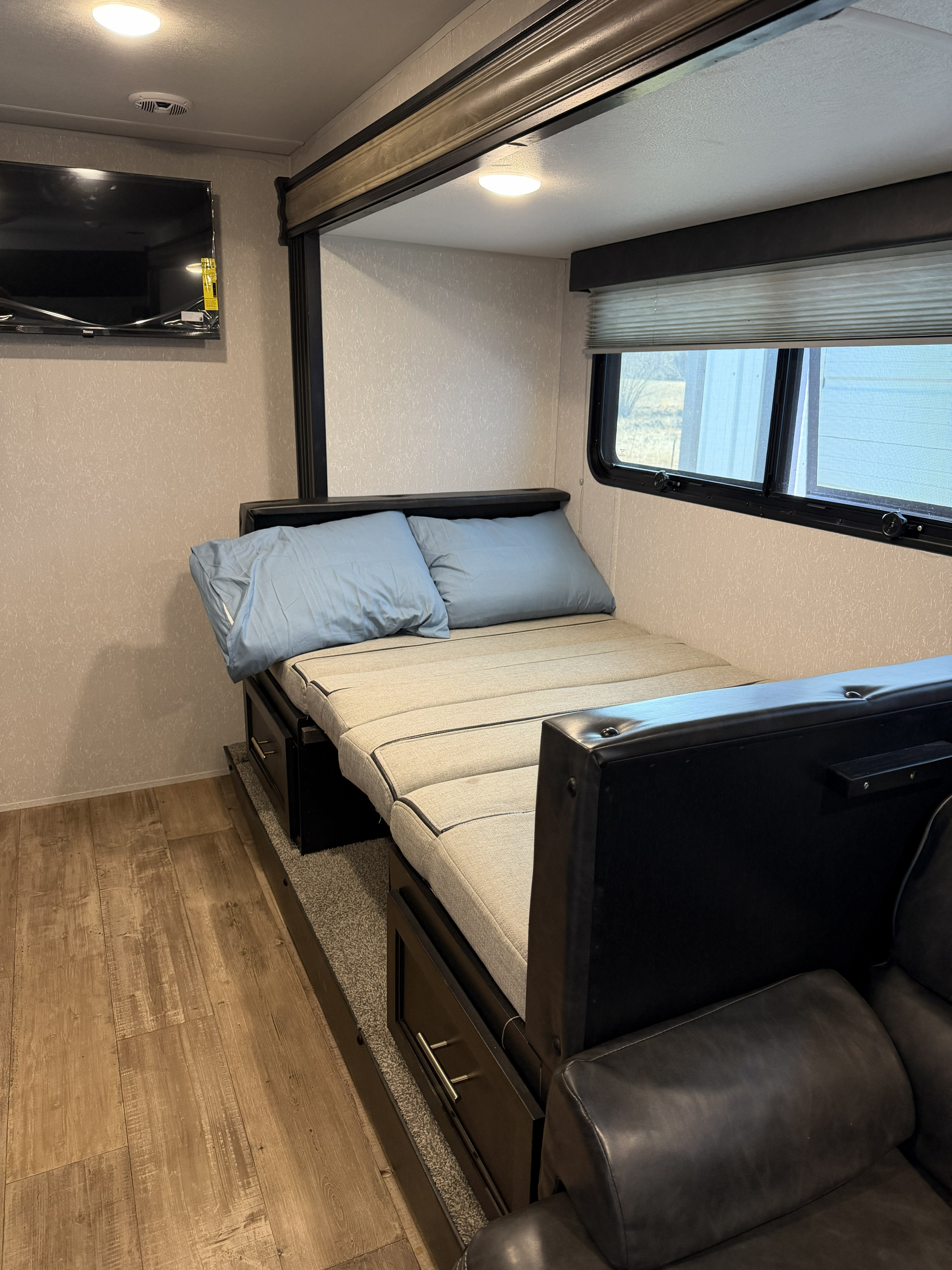 Inside an RV rental: sofa converted to a bed with pillows, wall-mounted TV, and window with blinds.. Forest River Cherokee Wolf Pup Black Label 2021