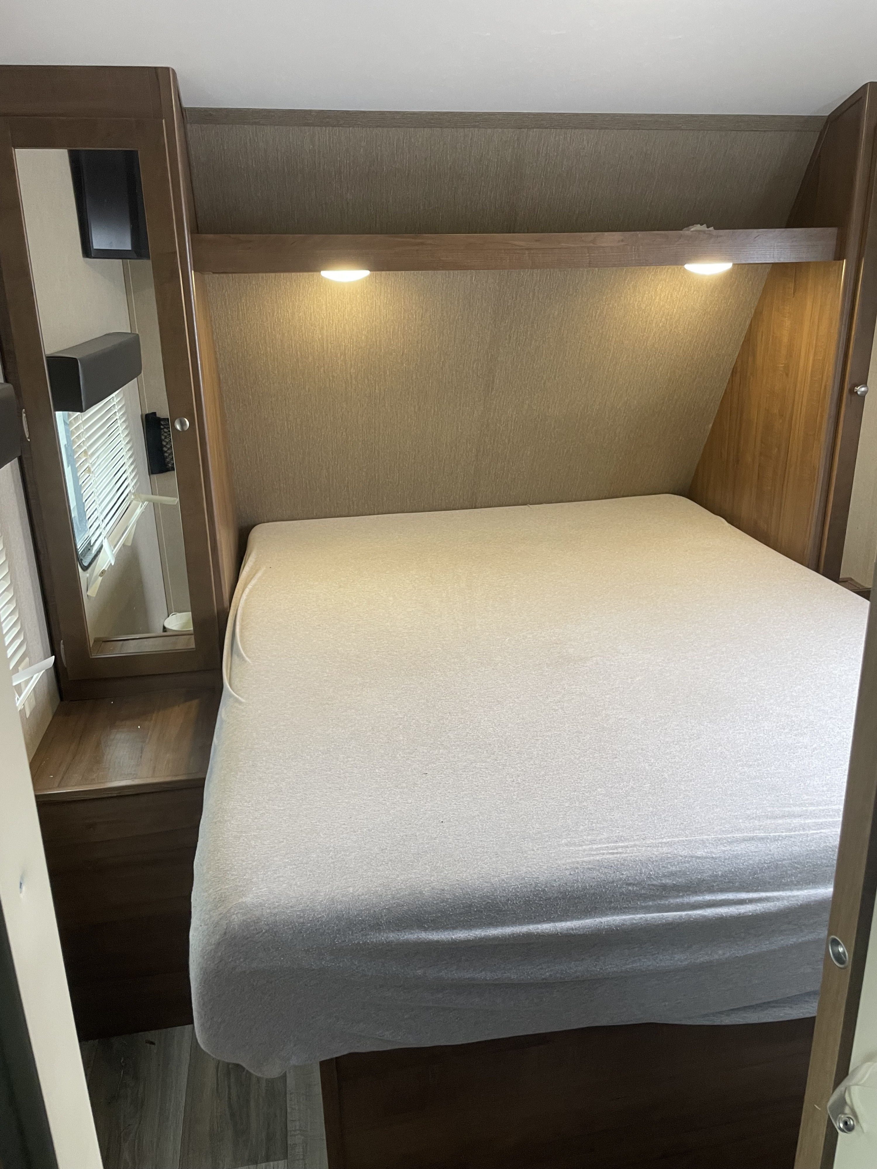 Cozy rv rental bedroom featuring a comfortable bed, overhead reading lights, a mirrored cabinet, and a window with blinds.. Aspen Trail Aspen Trail Trailer 2017