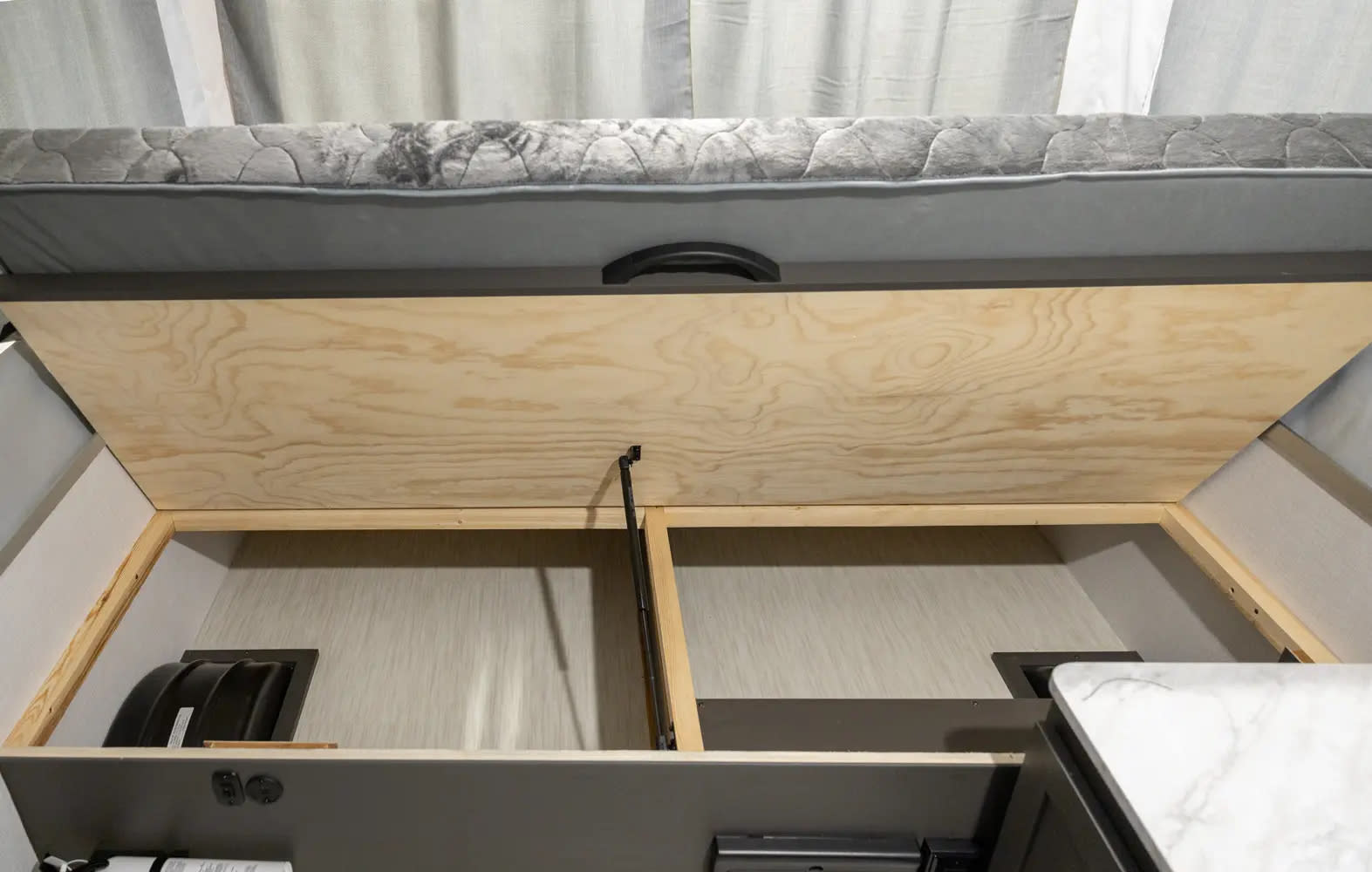 RV rental under-bed storage area, lifted to reveal compartments. Perfect for organizing camping essentials in your travel trailer.. Forest River OTG 2025