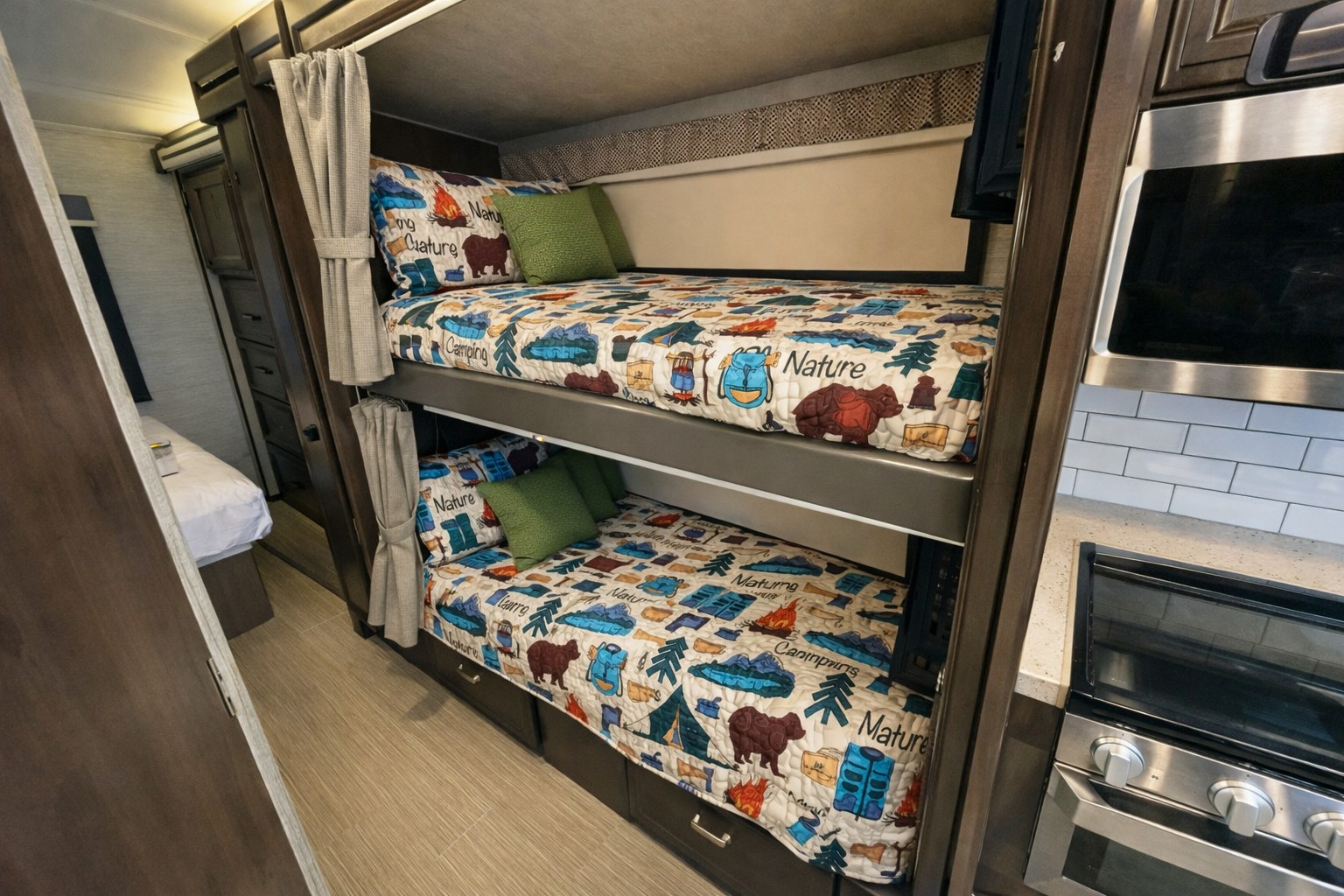 RV rental with cozy bunk beds featuring camping-themed bedding and green pillows, adjacent to a compact kitchen.. Entegra Coach Esteem 2021