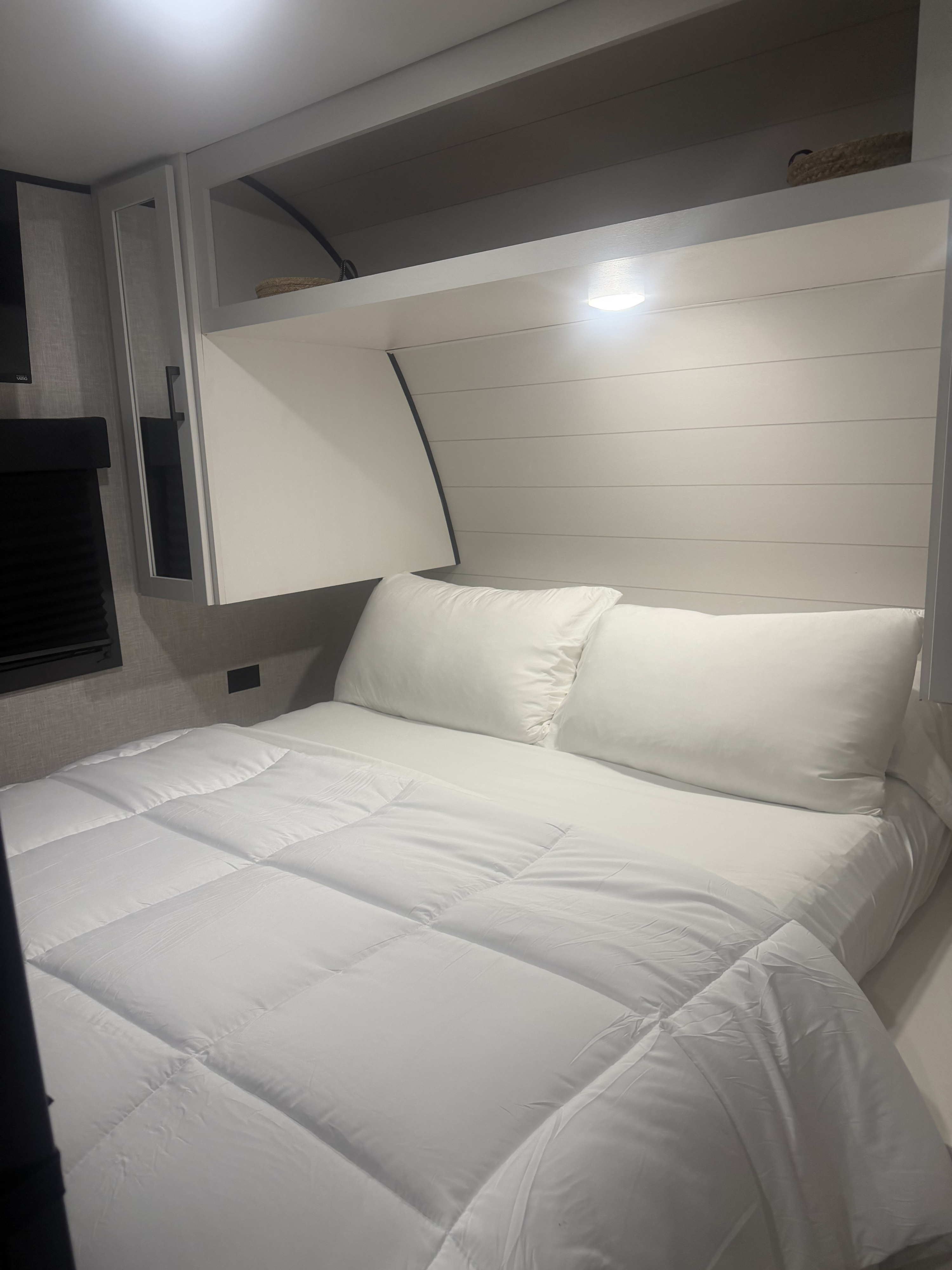 Cozy rv rental bedroom features a neatly made bed with white bedding, pillows, overhead storage, and shiplap headboard.. Highland Ridge RV Open Range 2025