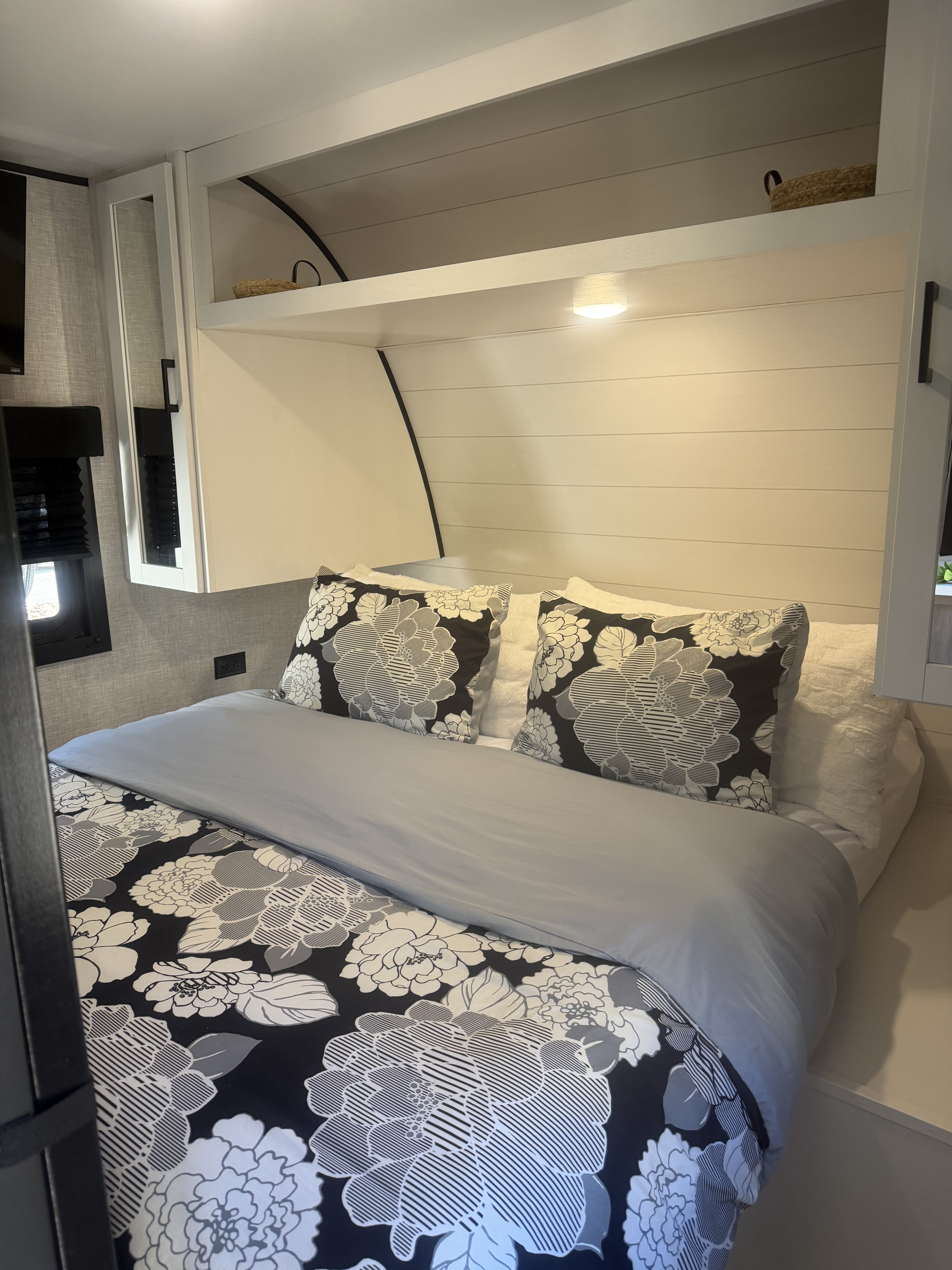 Cozy RV rental bedroom featuring a bed with elegant floral bedding, decorative pillows, shiplap headboard, and overhead storage.. Highland Ridge RV Open Range 2025