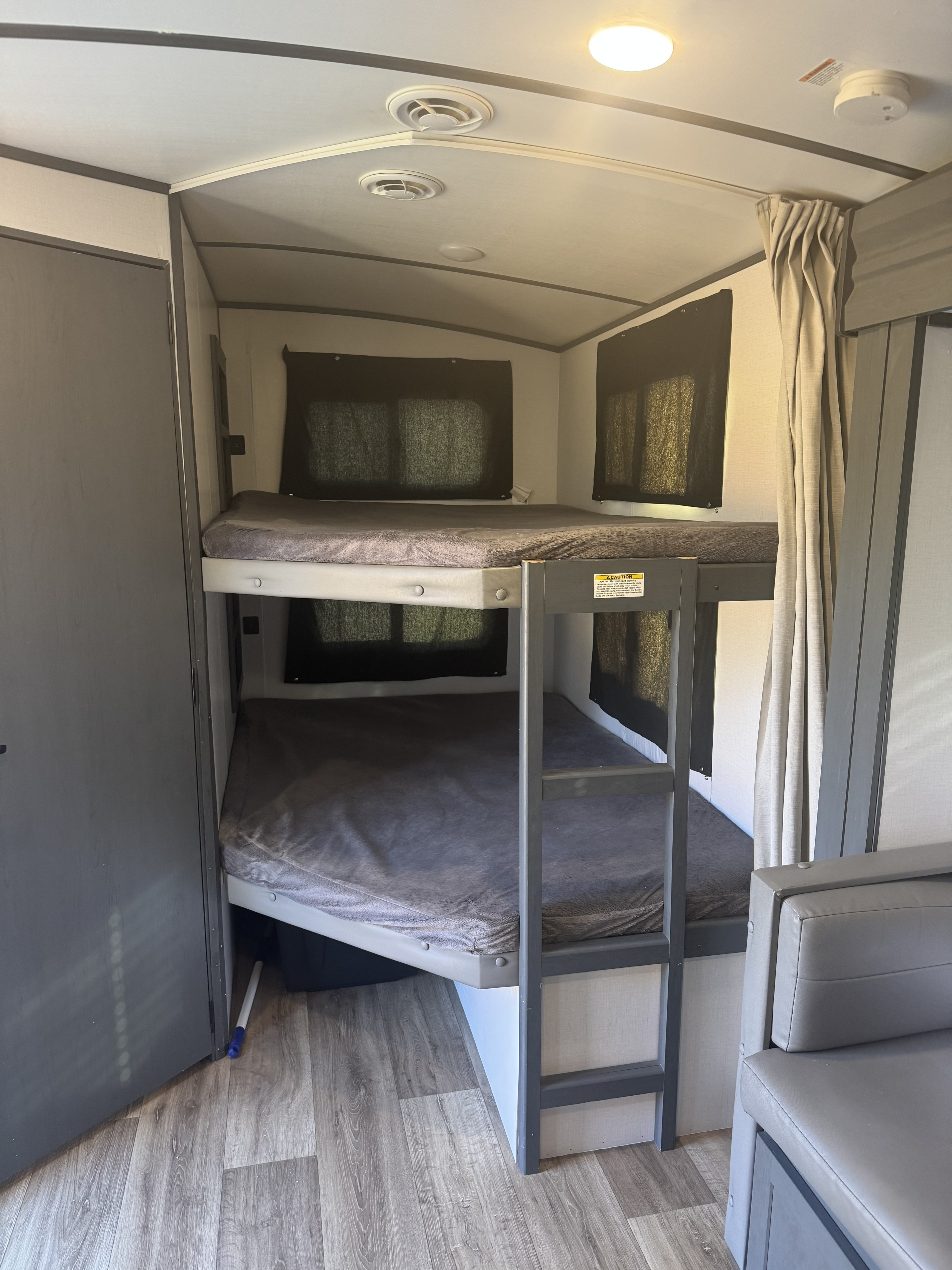 Inside an rv rental, spacious bunk beds with grey bedding, dark window blinds, and a built-in ladder for comfortable sleep.. Keystone RV Bullet Ultra Lite 2022