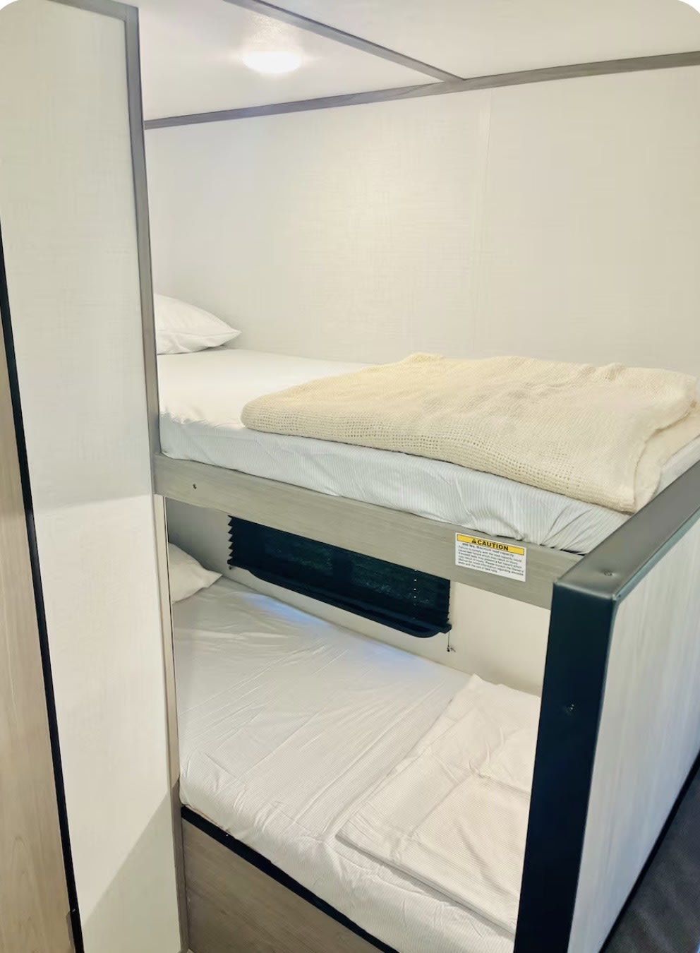 Cozy RV rental bunk beds with clean white bedding, a light blanket on the top bunk, and privacy shades for comfortable sleep.. Keystone RV Coleman 17B 2024