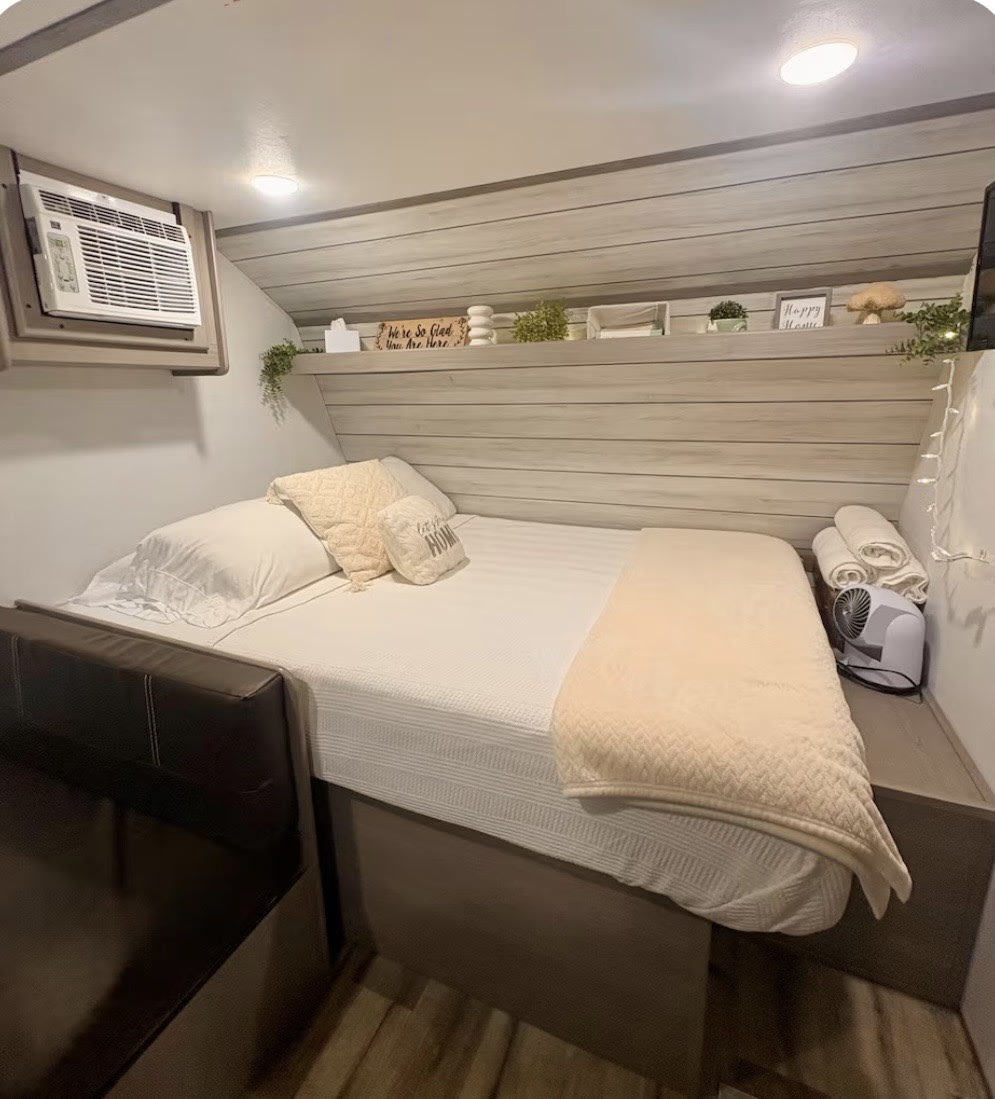 Cozy RV rental bedroom with white bedding, decorative shelf, and AC unit. Perfect for comfortable travel accommodation.. Keystone RV Coleman 17B 2024