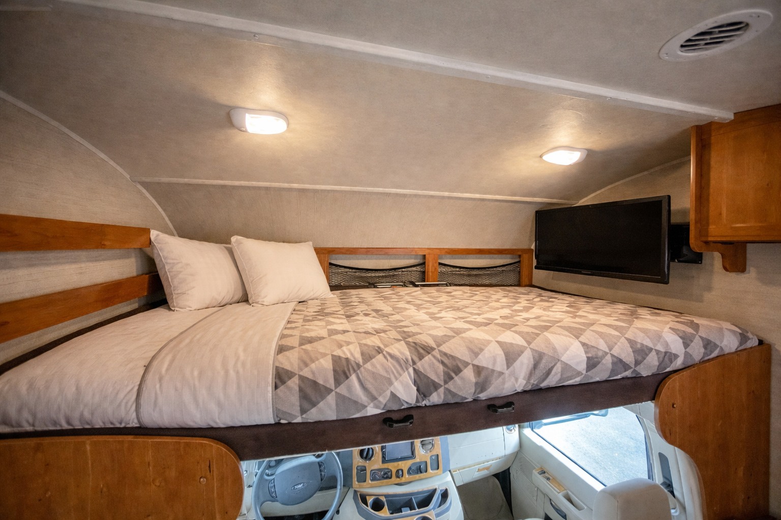 Cozy RV rental cab-over bunk bed setup with pillows, quilt, TV & dashboard view below for comfortable travel.. Jayco Redhawk 2017