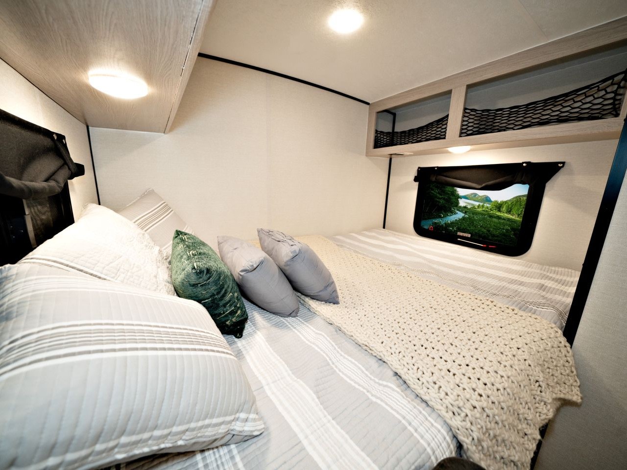 This RV rental bedroom offers a comfortable bed with pillows, overhead storage, and a virtual window with a scenic view.. Forest River Coachman apex 16 2022