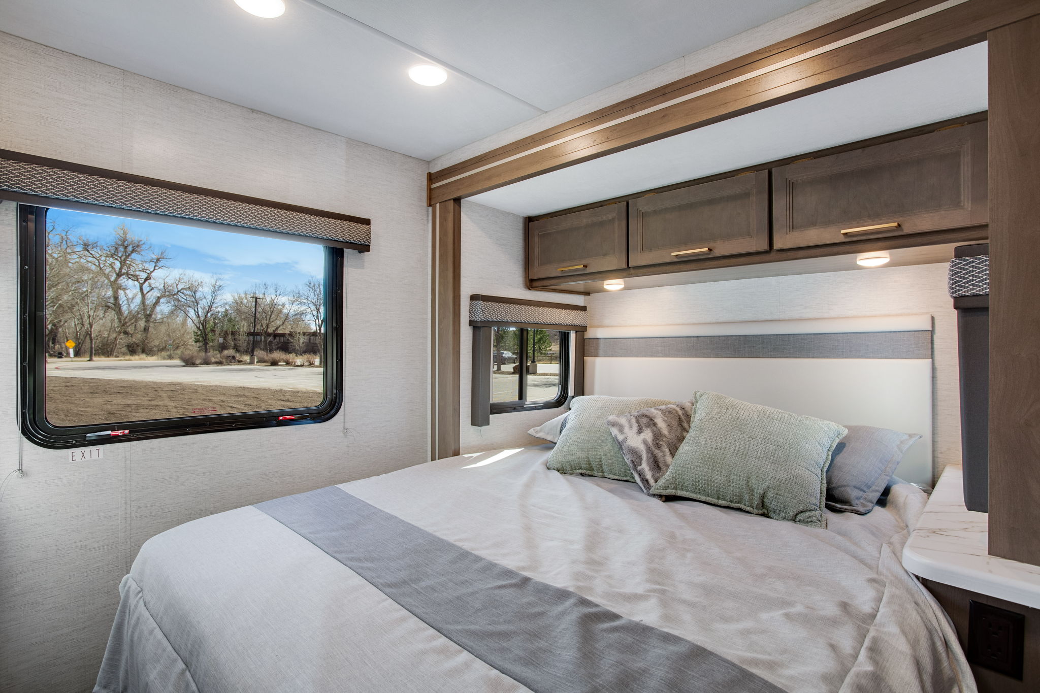 Spacious RV rental bedroom with a comfy bed, scenic window view, and overhead storage, perfect for your next adventure.. Thor Four Winds 2025