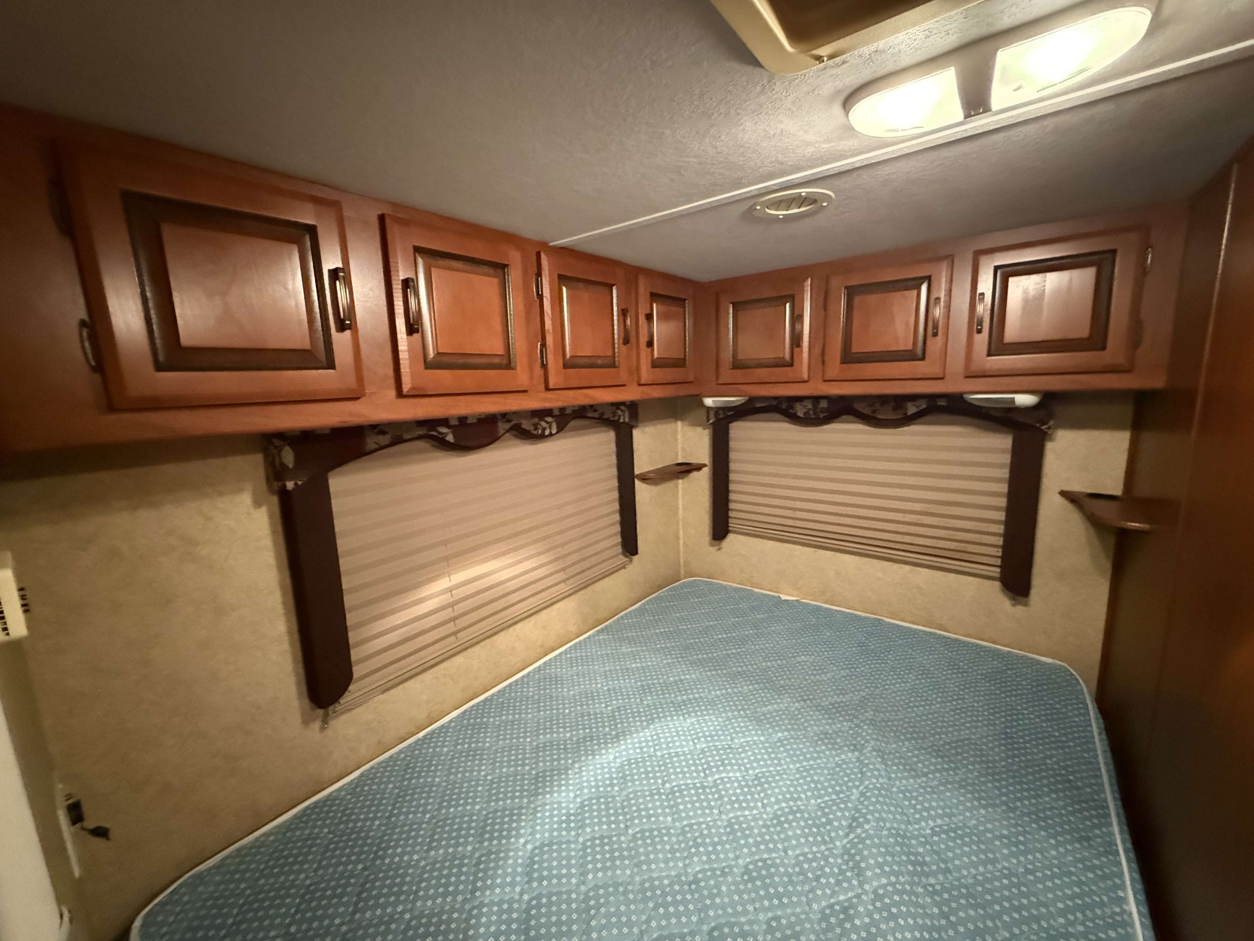 Cozy RV rental bedroom featuring a blue mattress, ample wood overhead cabinets, and window blinds for privacy.. Forest River Sunseeker 2010