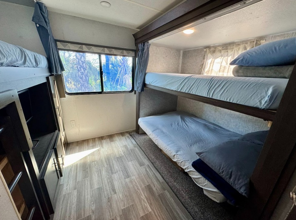RV rental's bunk beds: Three cozy berths with light blue bedding, a window with outdoor views, and wood-look flooring.. Salem 32BHDS 2020