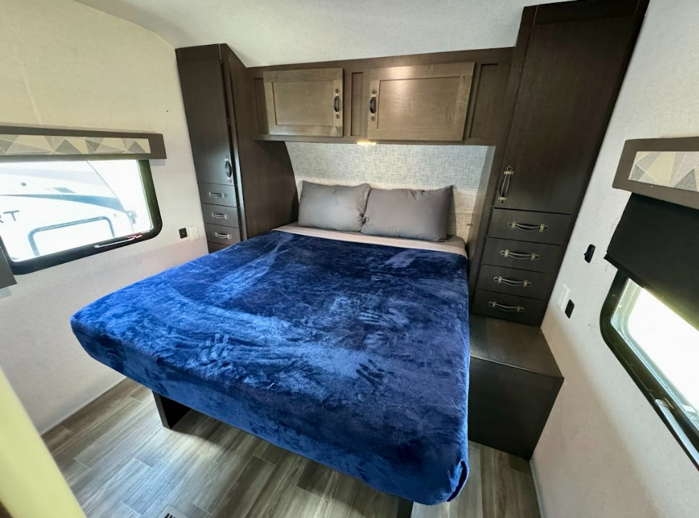 RV rental bedroom features a blue bed, grey pillows, overhead cabinets, and side storage for comfortable travels.. Salem 32BHDS 2020