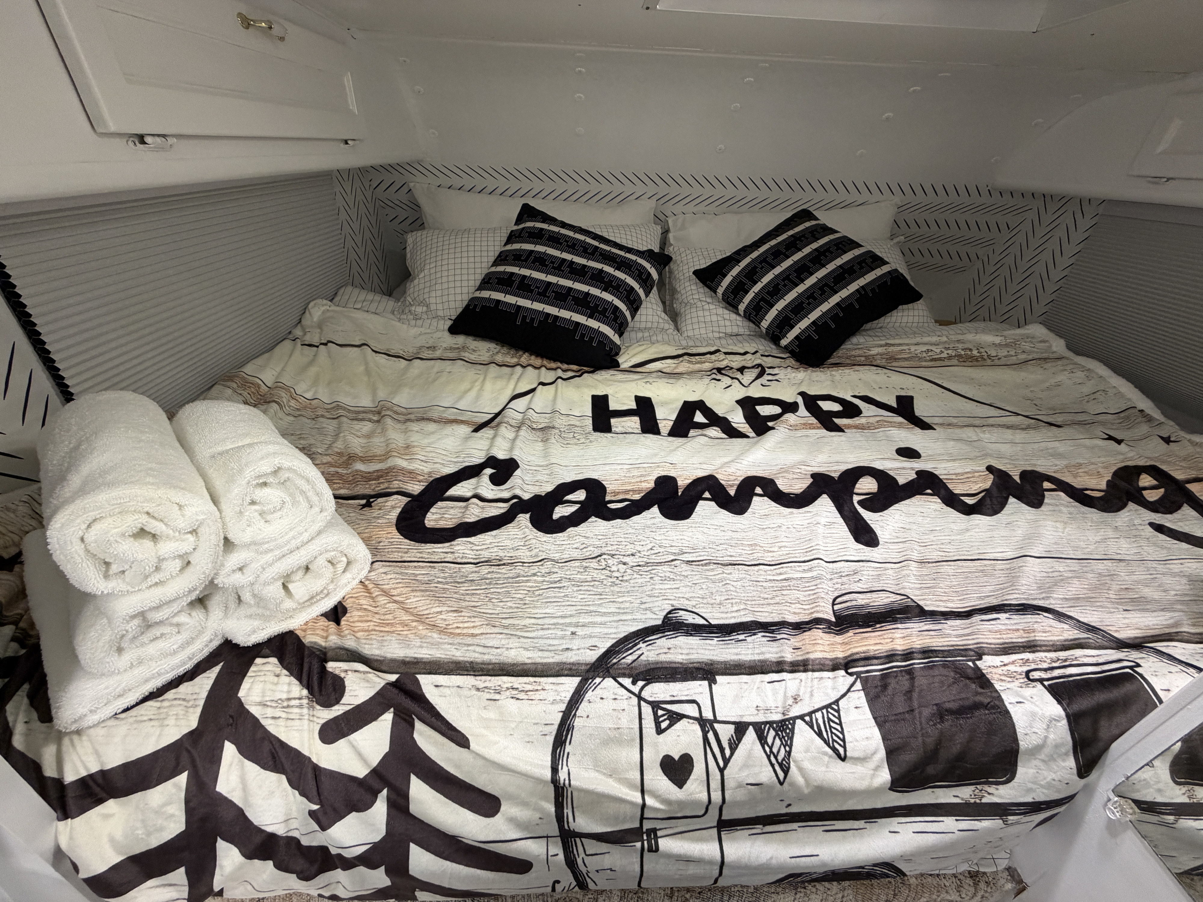 Cozy RV rental bed with "Happy Camping" duvet, black & white pillows, and white rolled towels. Ready for your trip!. Western Rv 2014 f150. 6 seats 1999