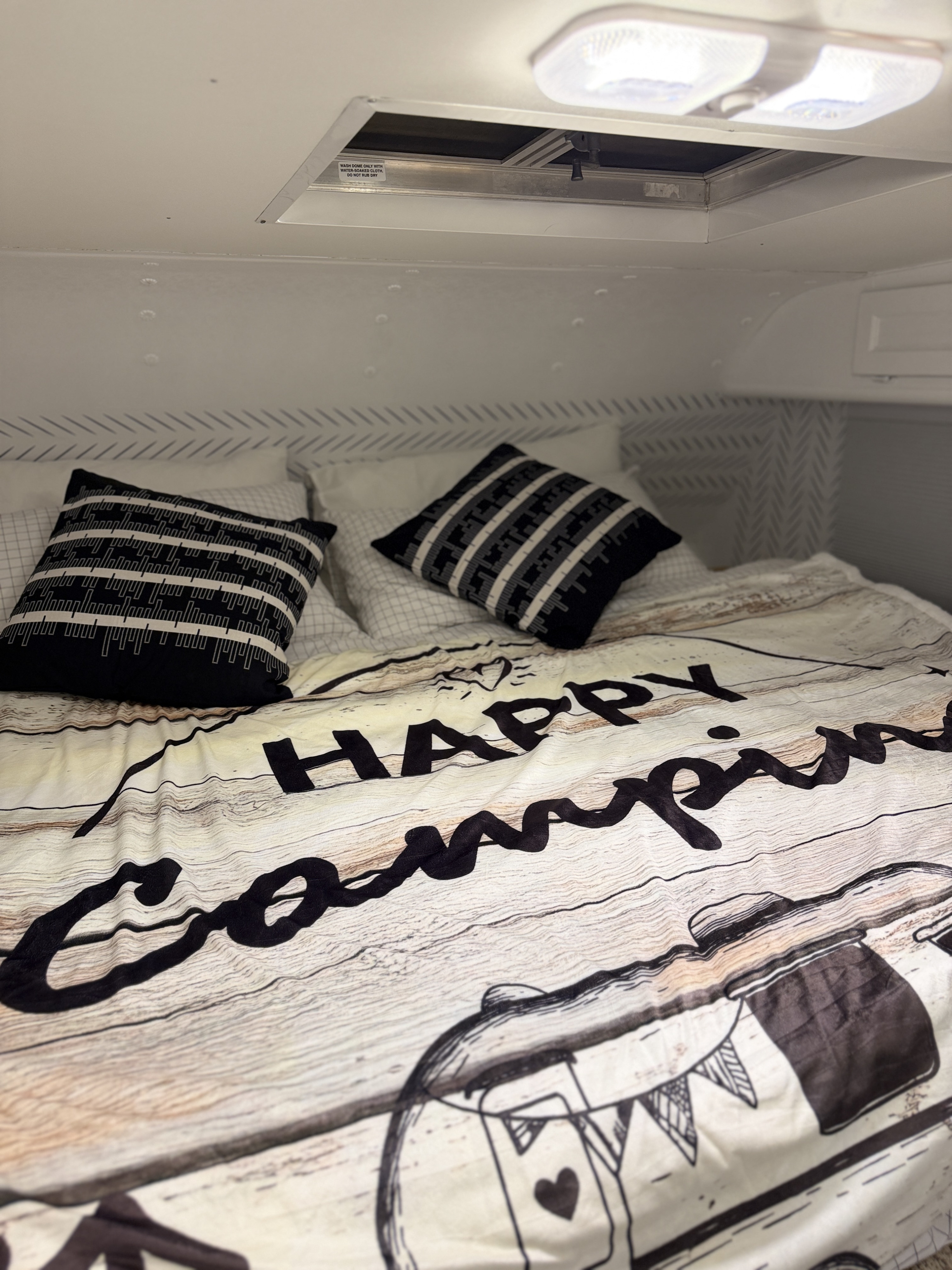 Cozy RV rental bedroom with a "Happy Camping" duvet and patterned pillows, ideal for a comfortable travel adventure.. Western Rv 2014 f150. 6 seats 1999