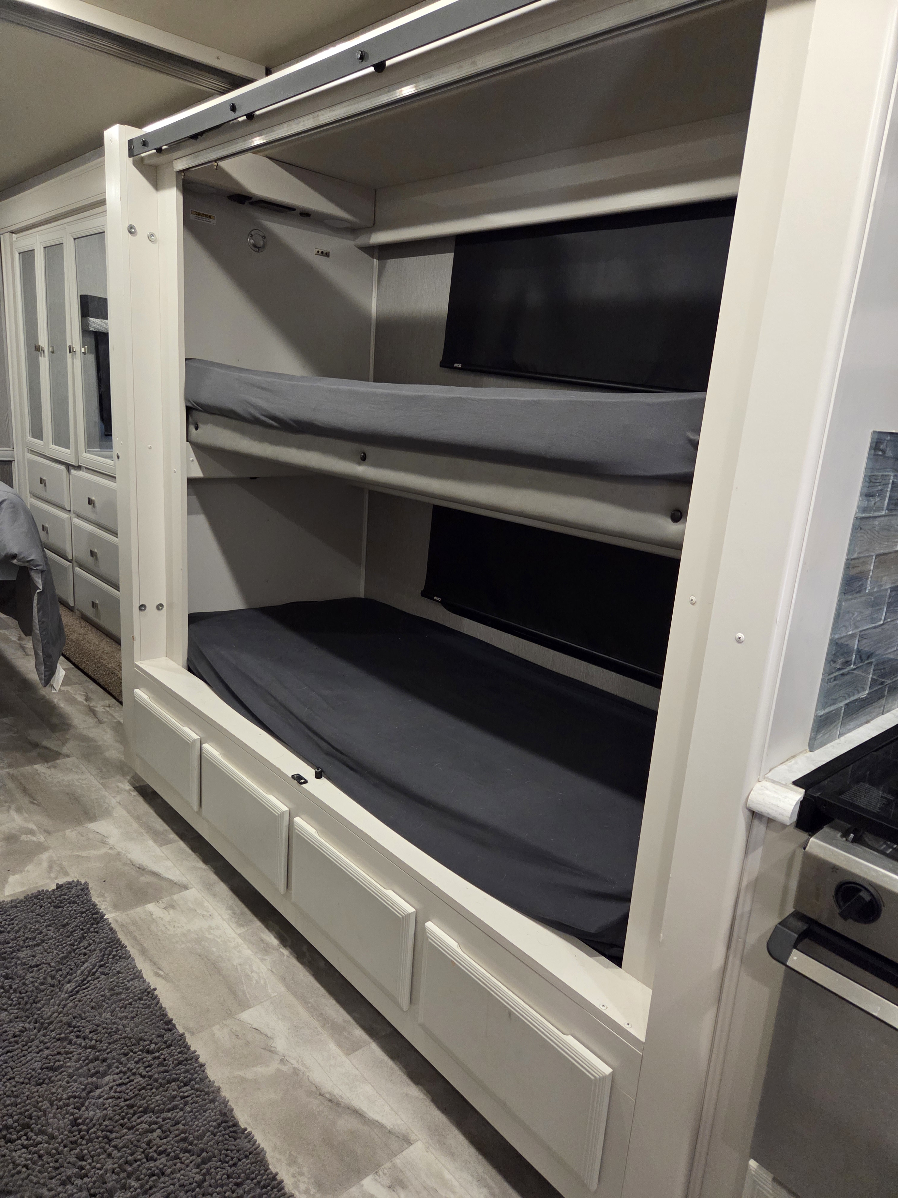 RV rental: Compact interior featuring two bunk beds with gray sheets, mirrored cabinets, and a kitchen stove on the right.. Fleetwood Flair 34J 2021