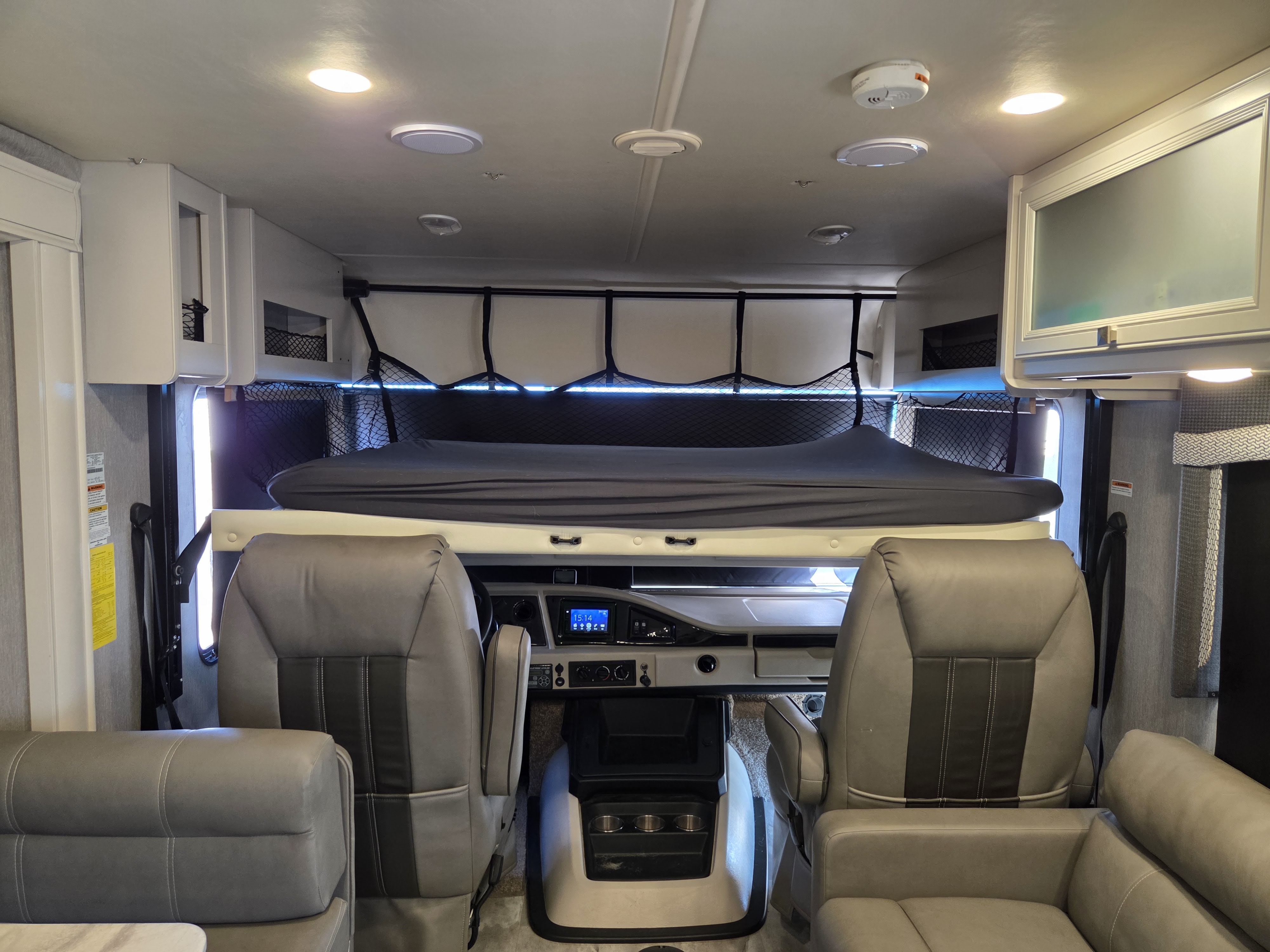 RV rental interior view showcasing front cabin with driver/passenger seats, dashboard, and an overhead bunk bed.. Fleetwood Flair 34J 2021
