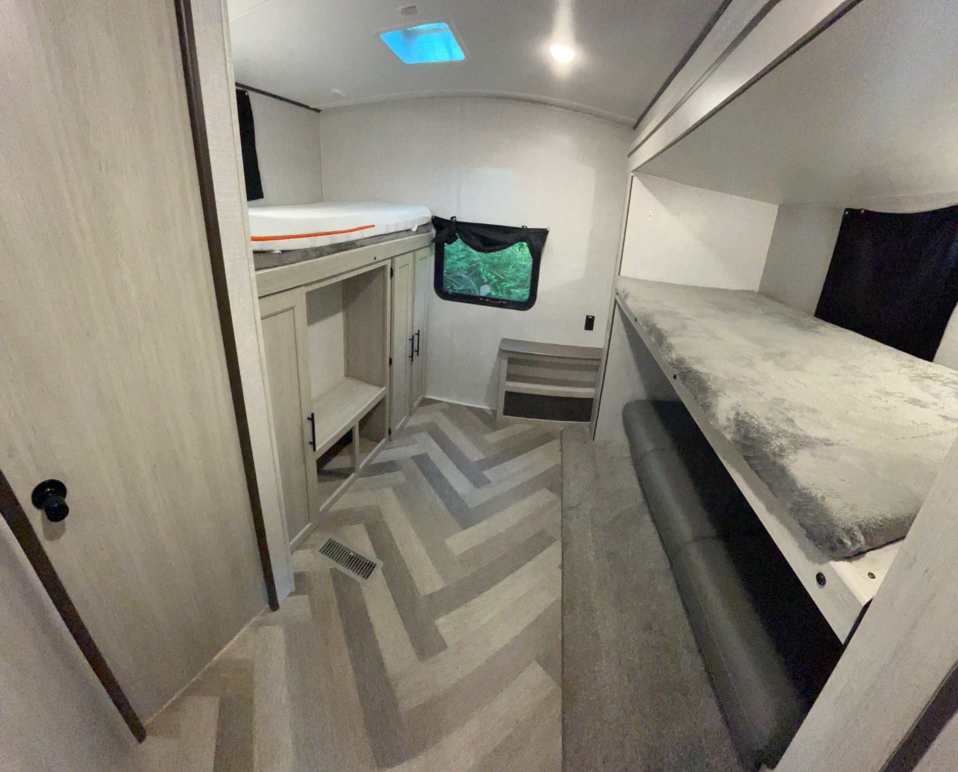 Spacious bunkhouse in an RV rental, featuring multiple bunk beds, storage, and a window with nature views.. Crossroads RV Zinger 2023