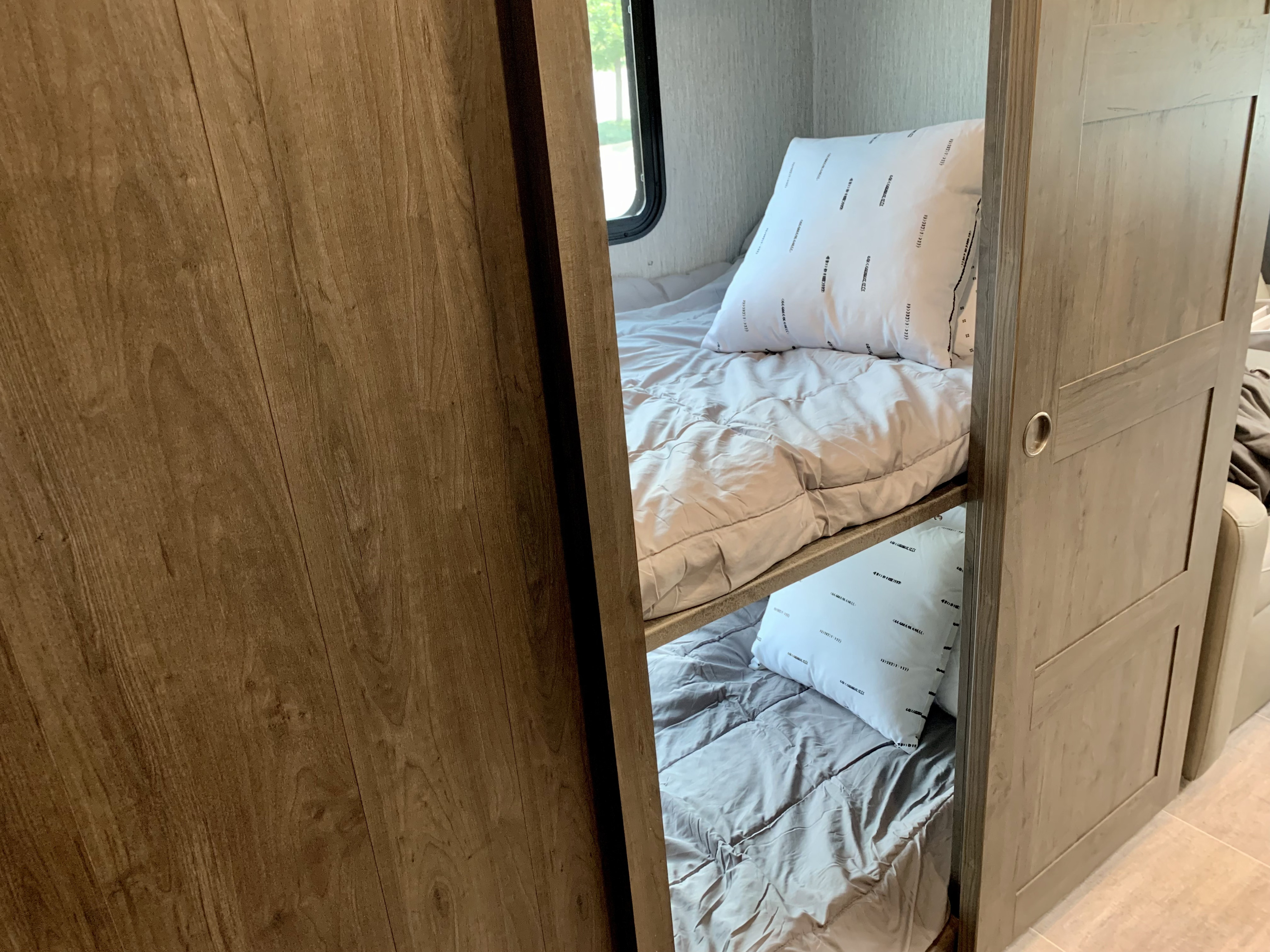 Cozy bunk beds in an RV rental, featuring light gray bedding and patterned pillows, framed by natural wood paneling.. Forest River Coachmen Mirada 2022
