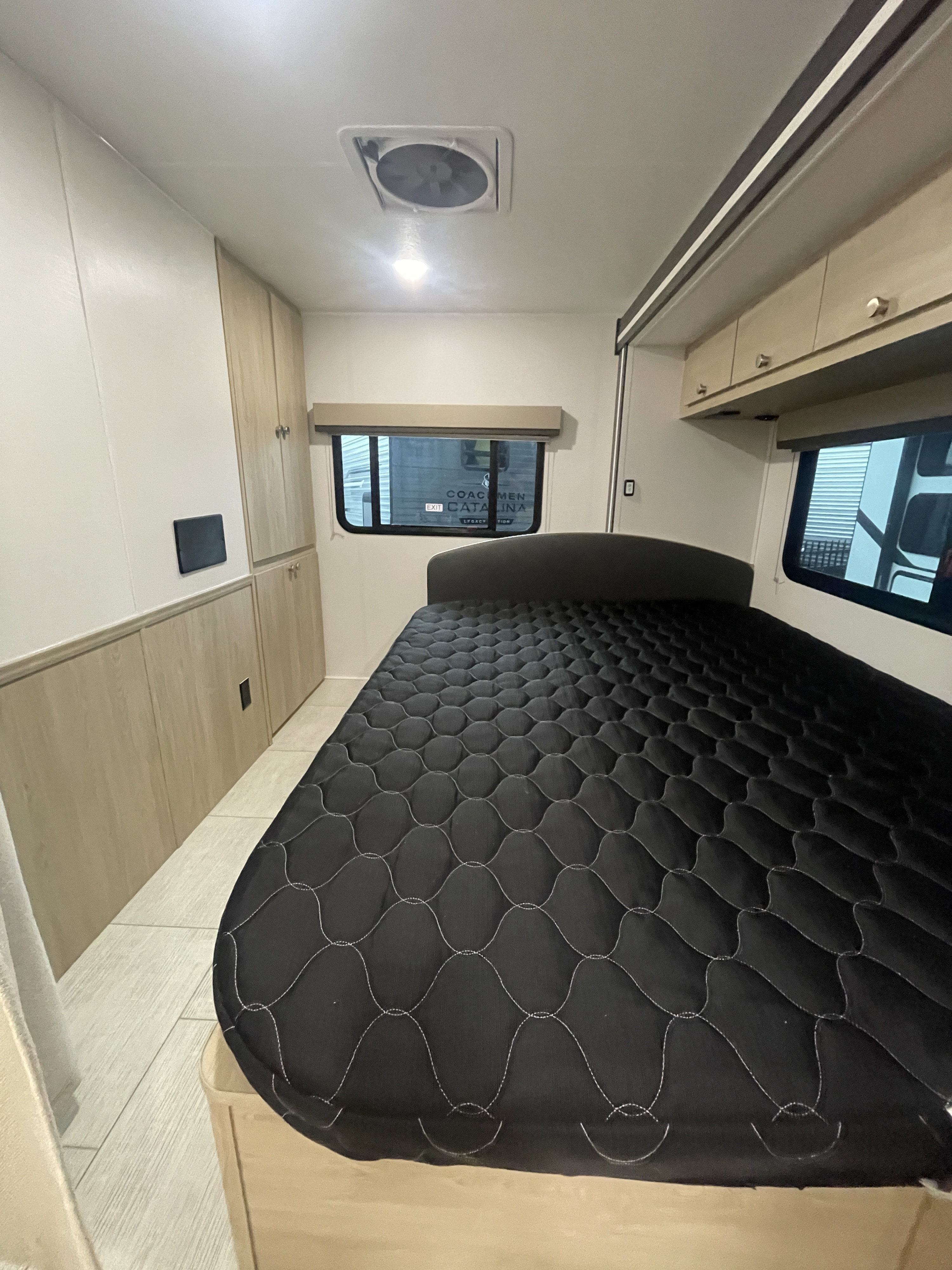 Spacious rv rental bedroom with a dark quilted mattress, light wood cabinets, a window, and a ceiling fan.. Coachmen LEPRECHAUN 230FS 2026